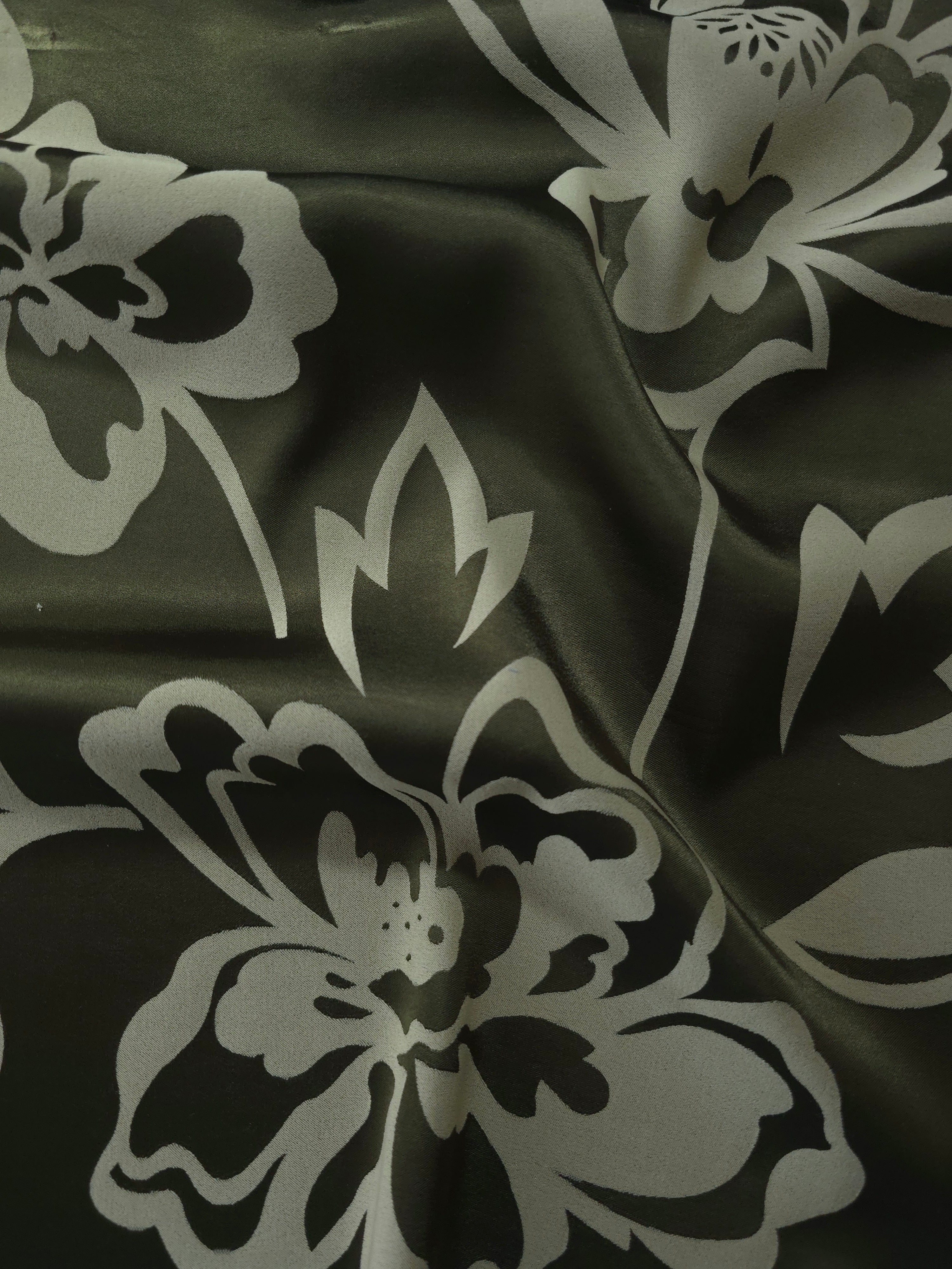 Forest green satin folded softly, the pale sage flower outline reading sharply against the darker base