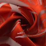 A tight fold in the orange-red satin, the ivory pattern lines bending visibly at the crease