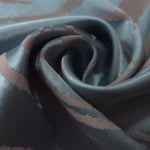 A tight fold in the slate blue satin, showing where the mauve pattern lines intersect near the crease