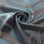 Slate blue Lassi satin hanging in soft waves, mauve seaweed lines visible across the moving fabric