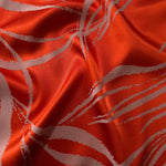Vivid orange-red satin folded over, the ivory seaweed lines standing out sharply against the bold base color