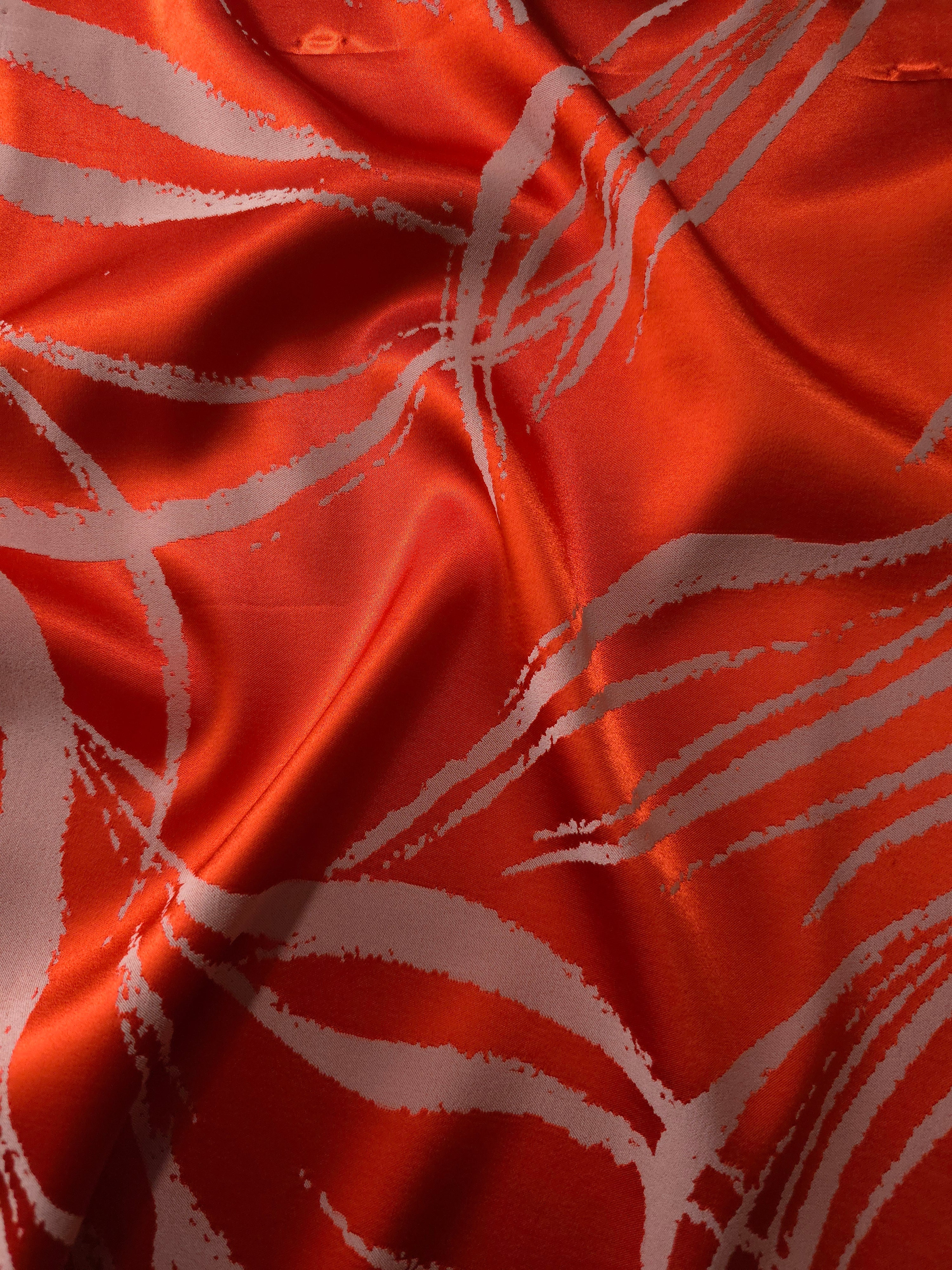 Vivid orange-red satin folded over, the ivory seaweed lines standing out sharply against the bold base color