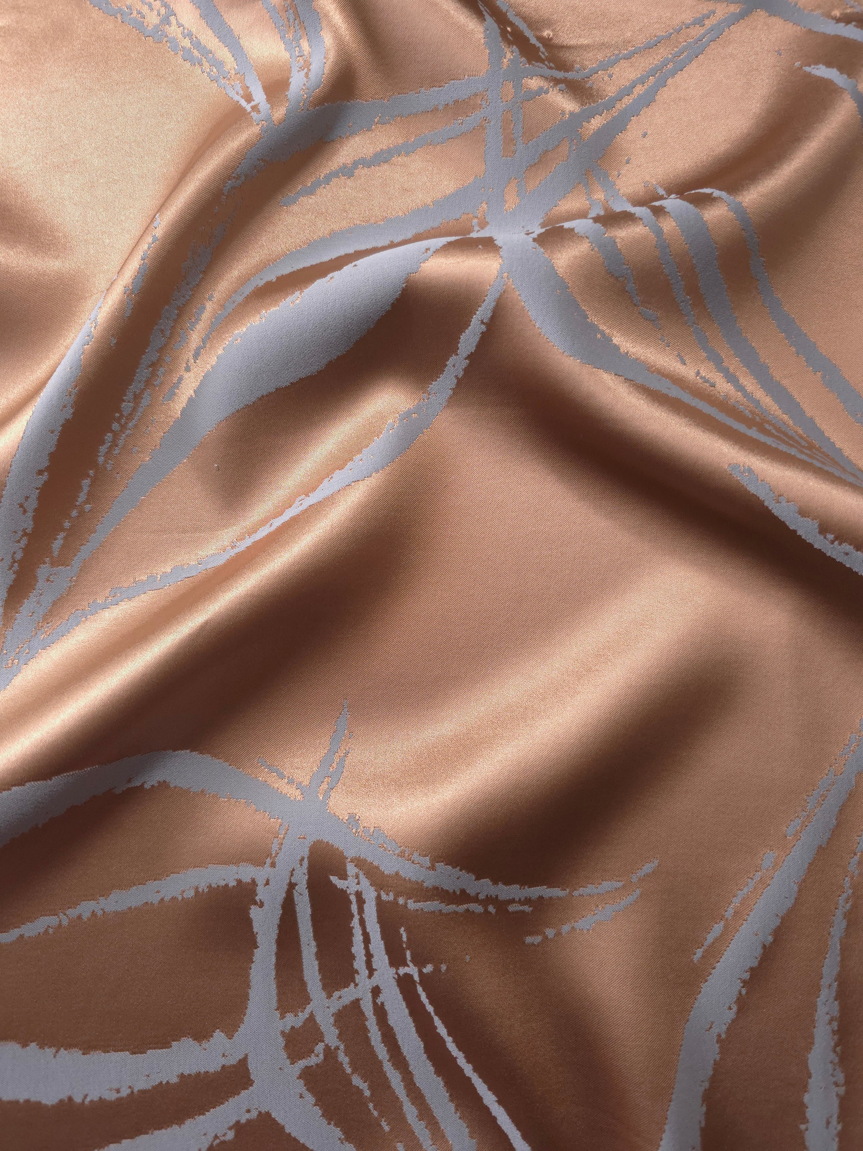 Copper-toned satin folded against itself, with the blue-grey seaweed lines crossing through the warm base color
