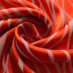 A tight fold in the orange-red satin, the ivory wave lines bending visibly with the crease