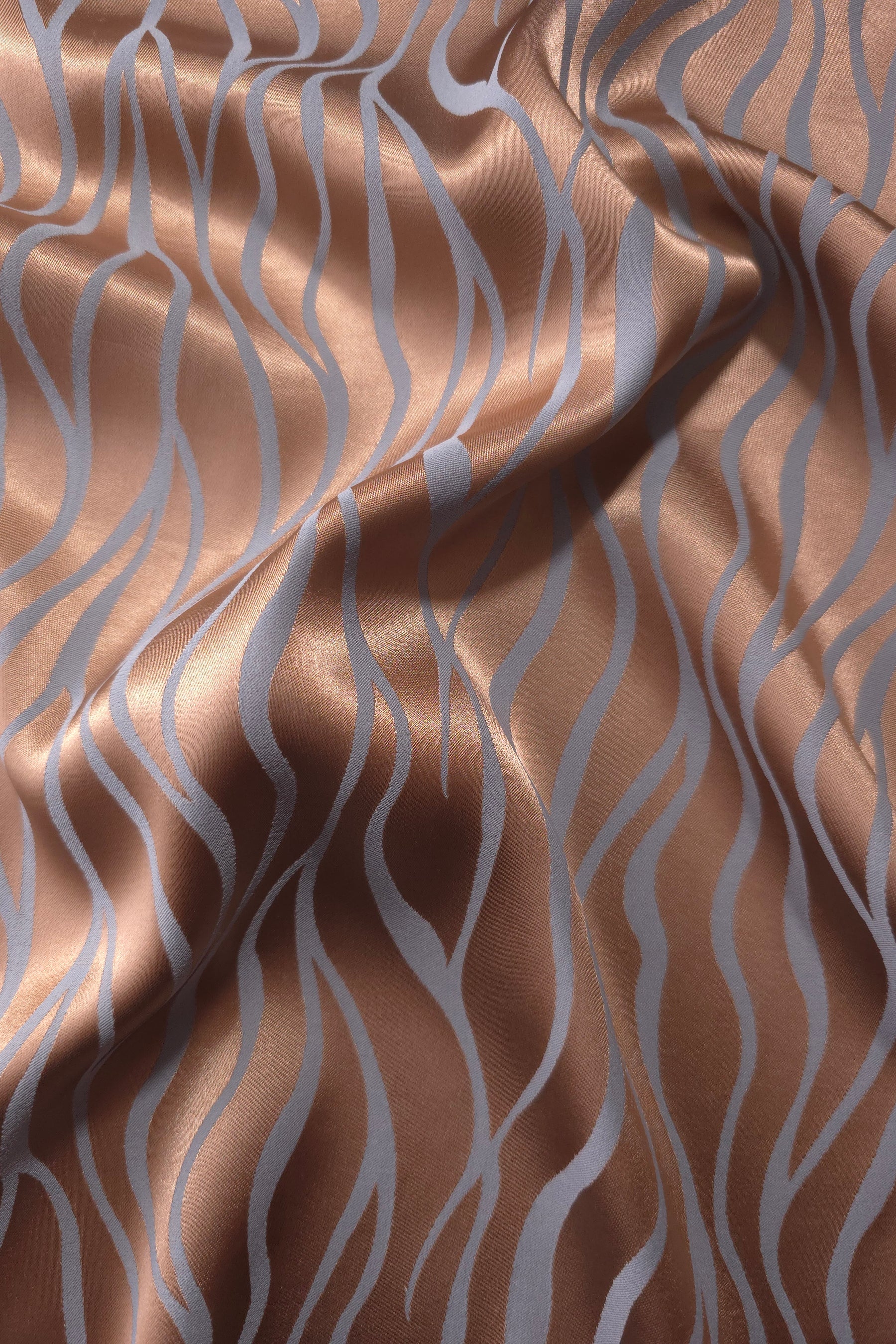 Copper Lassi satin folded over itself, the wave lines shifting between warm copper and cool blue-grey as the light moves