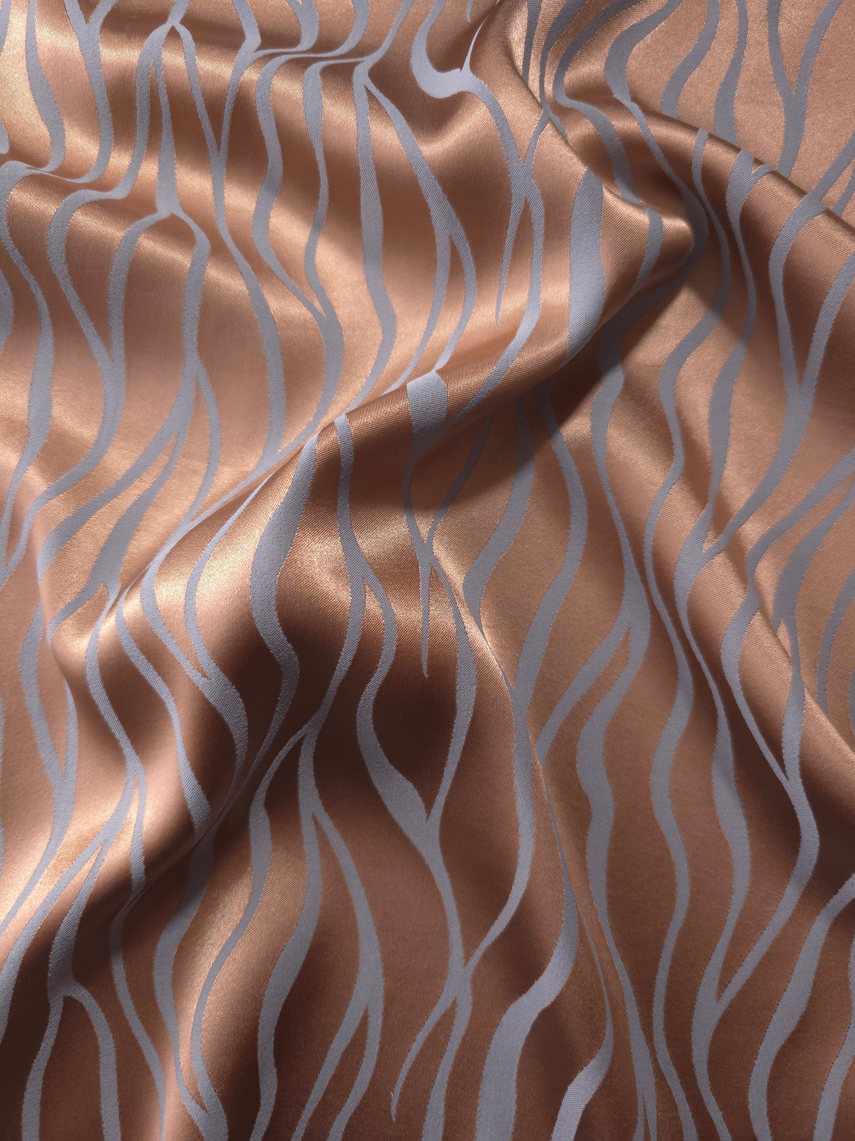 Copper Lassi satin folded over itself, the wave lines shifting between warm copper and cool blue-grey as the light moves