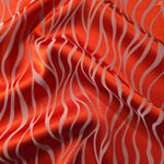 Vivid orange-red satin folded over, with pale ivory wave lines standing out sharply against the bold base color