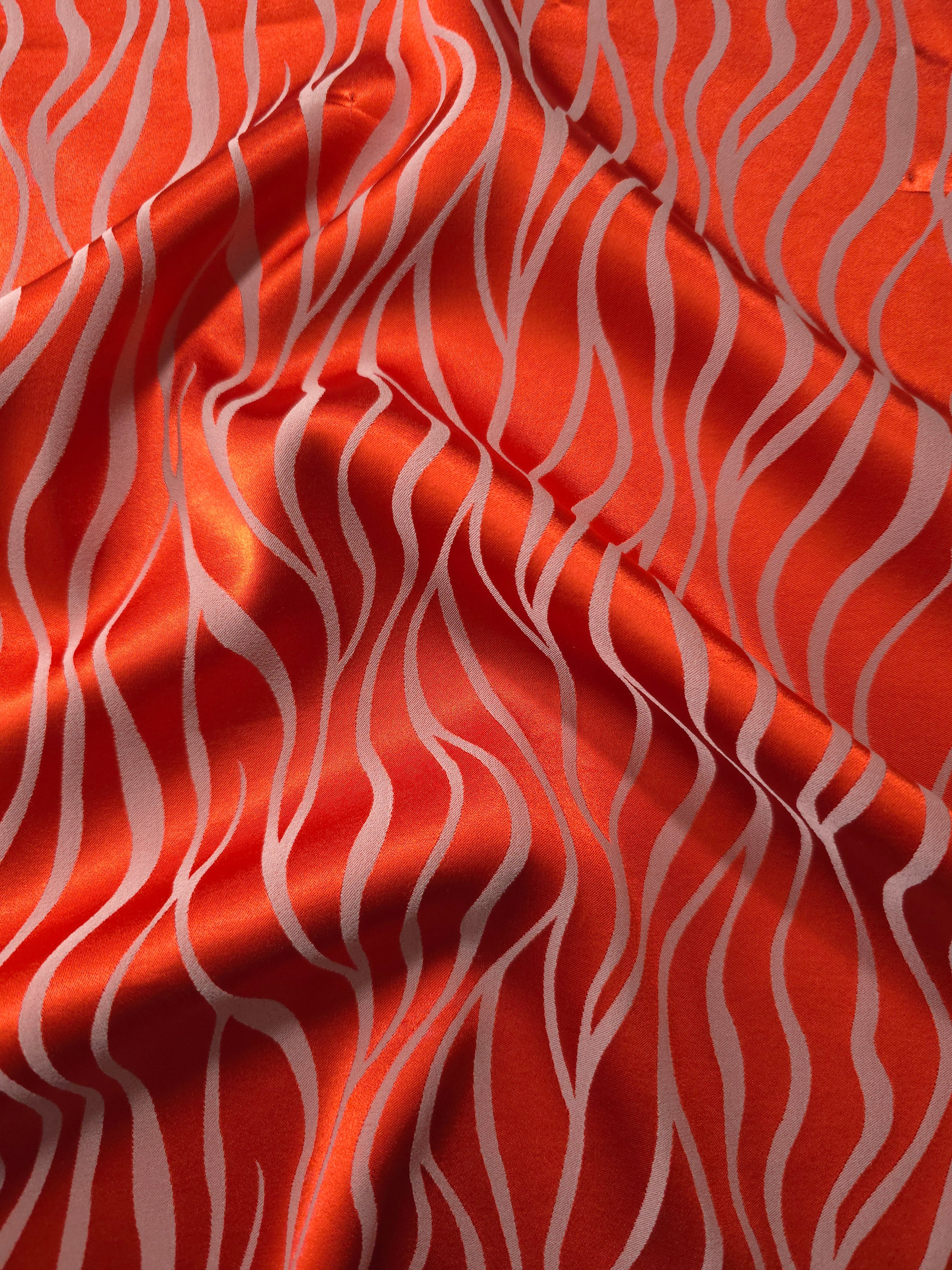 Vivid orange-red satin folded over, with pale ivory wave lines standing out sharply against the bold base color
