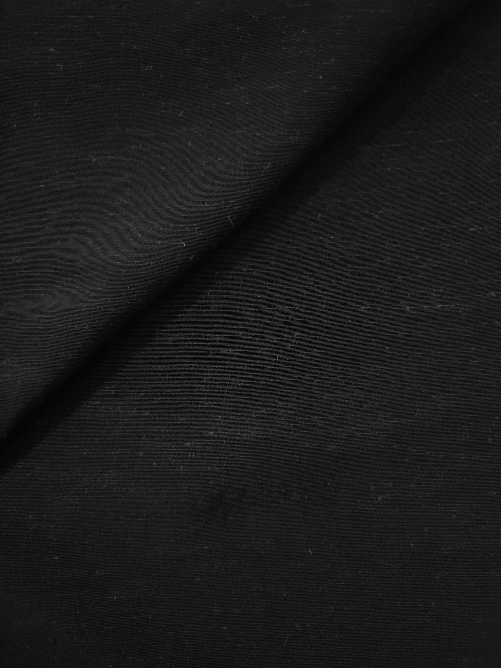 Close-up of deep black linen viscose plain fabric showing its natural woven texture.