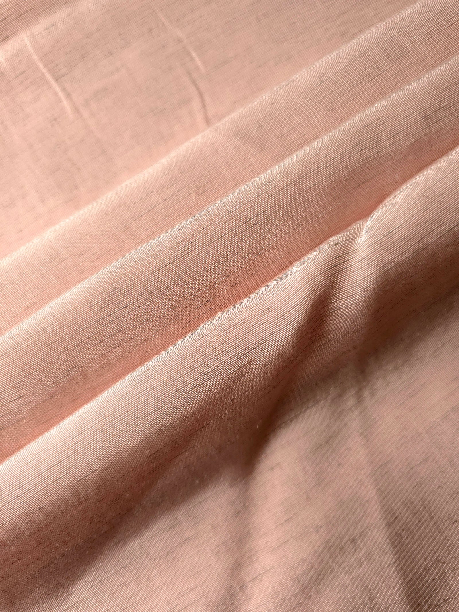 Folded delicate blush pink linen viscose plain fabric, illustrating its lightweight feel for garment sewing.