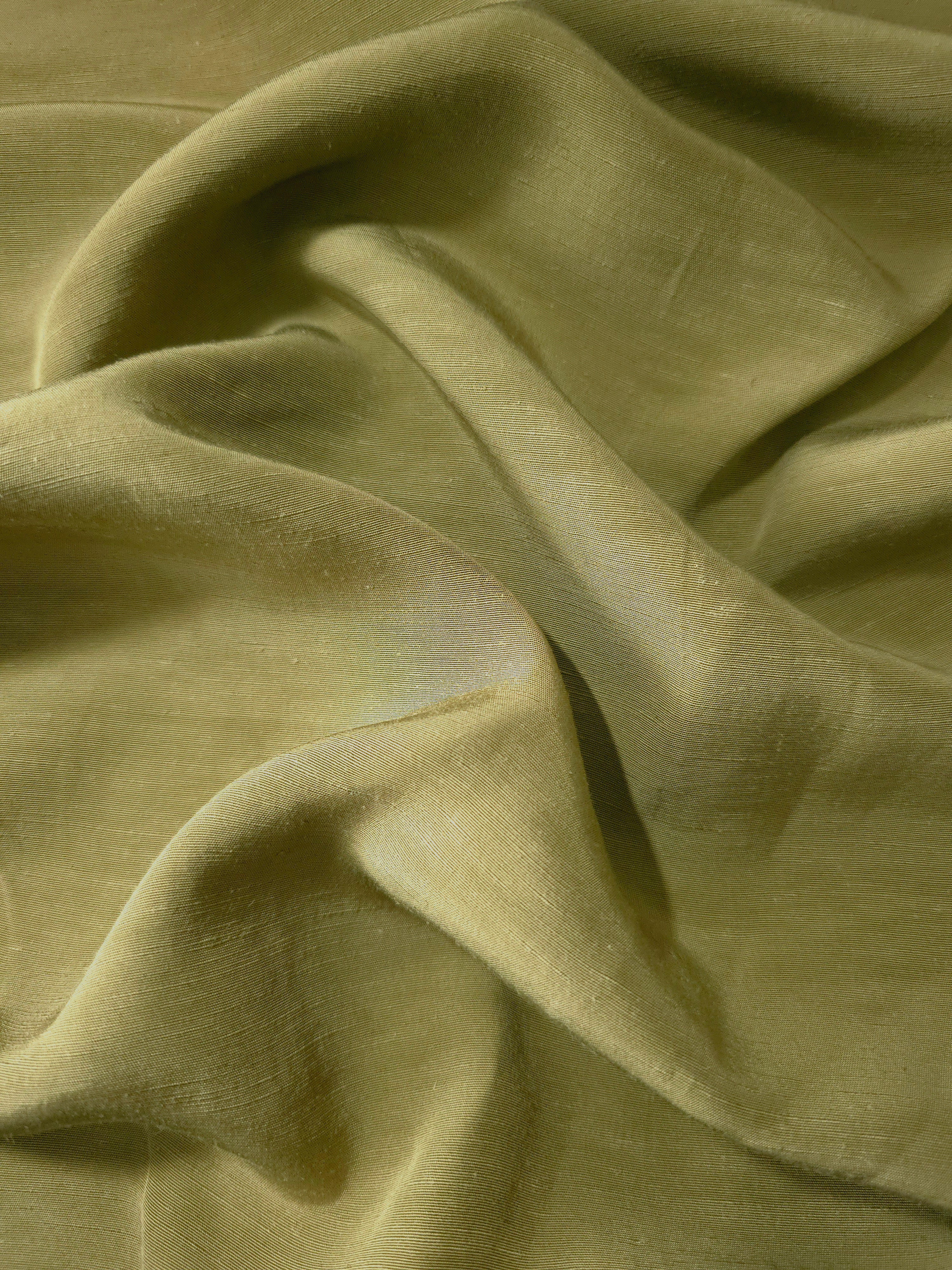 Close-up of fresh apple green linen viscose plain fabric showing its natural woven texture.
