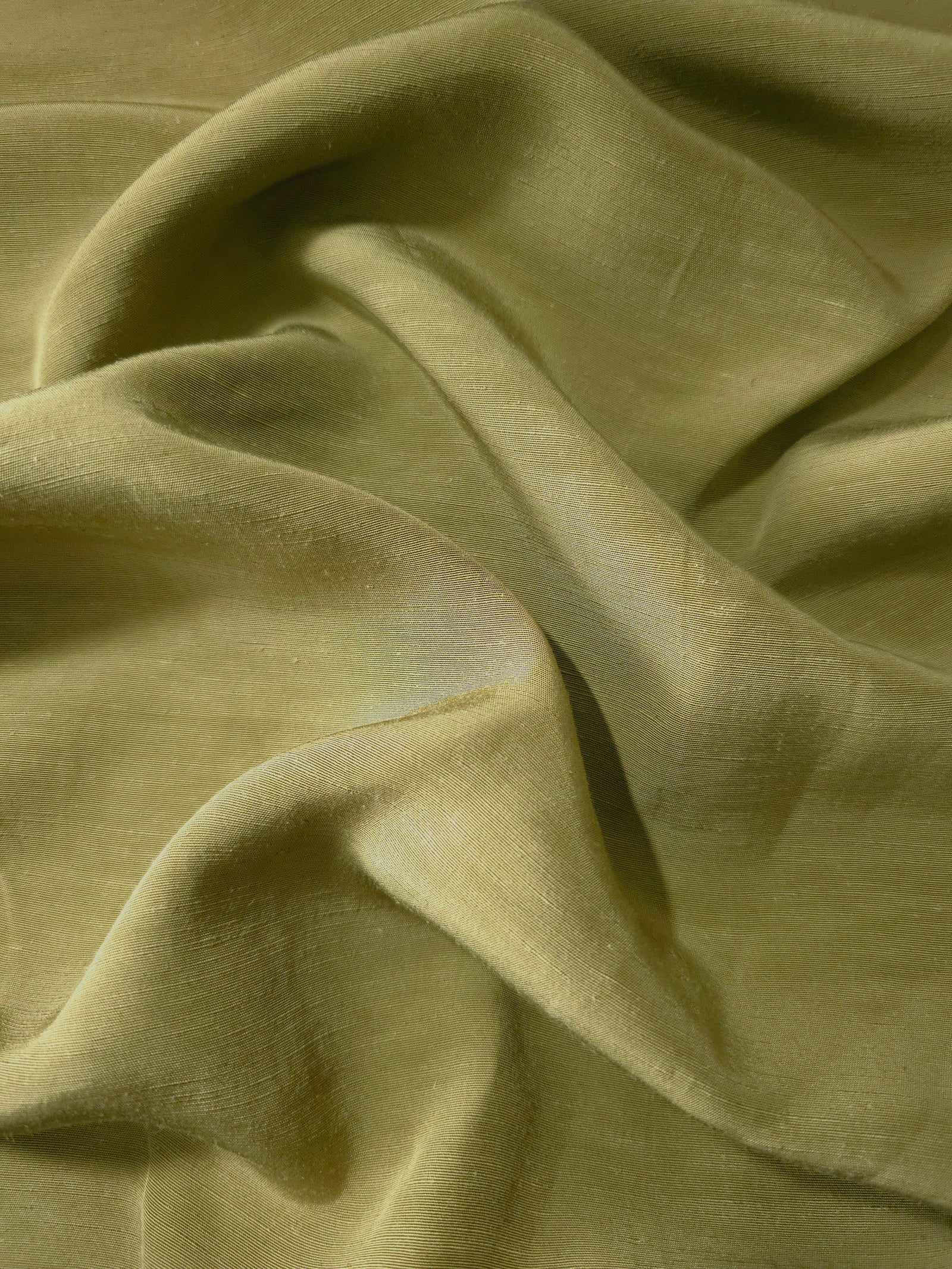 Close-up of fresh apple green linen viscose plain fabric showing its natural woven texture.