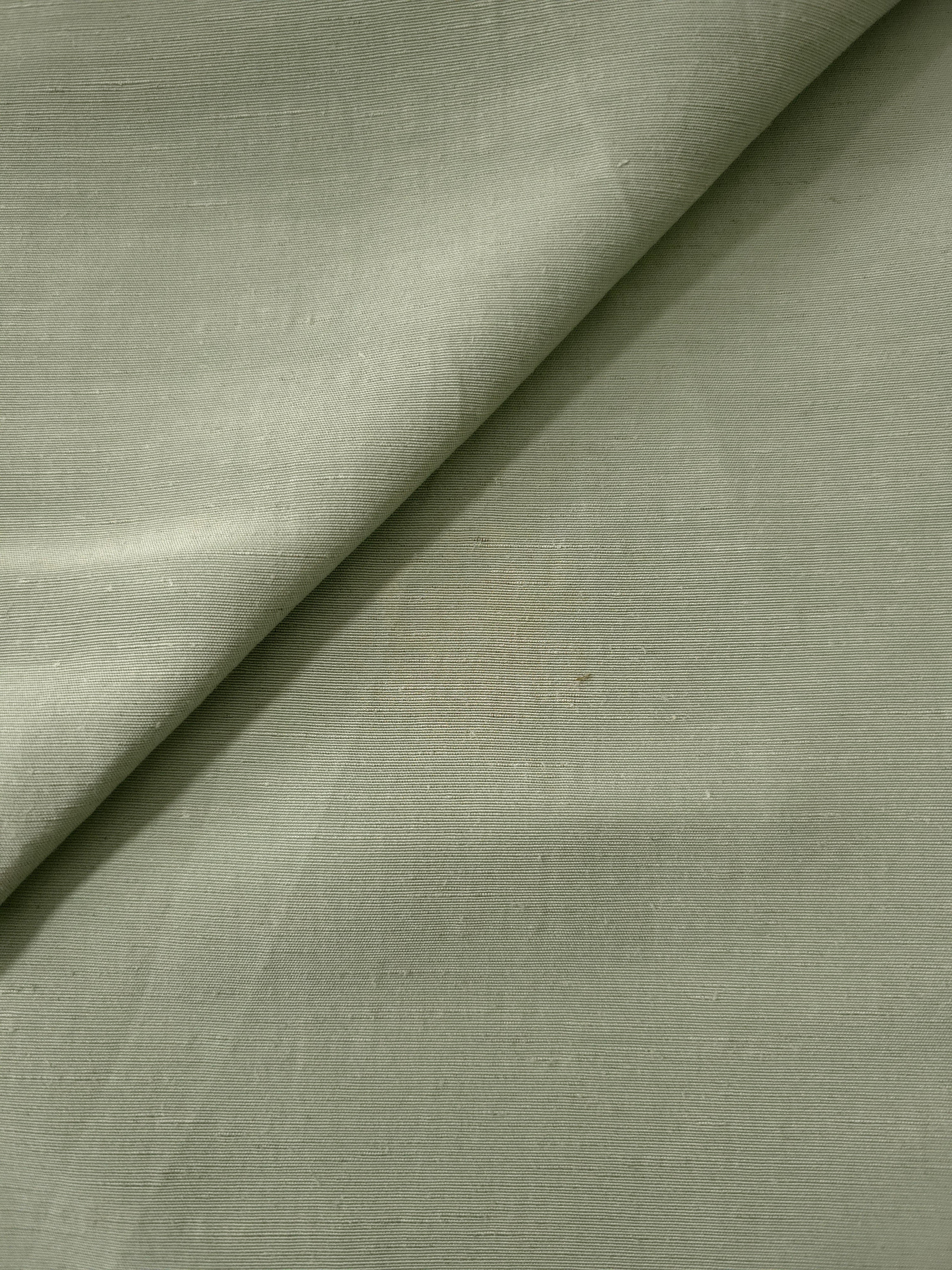 Close-up of muted sage grey linen viscose plain fabric showing its natural woven texture.
