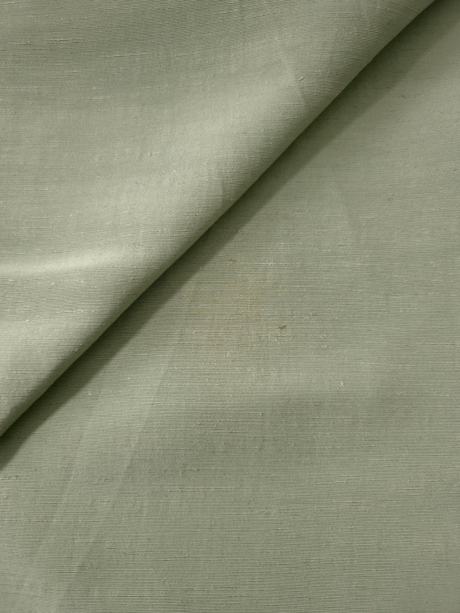 Close-up of muted sage grey linen viscose plain fabric showing its natural woven texture.