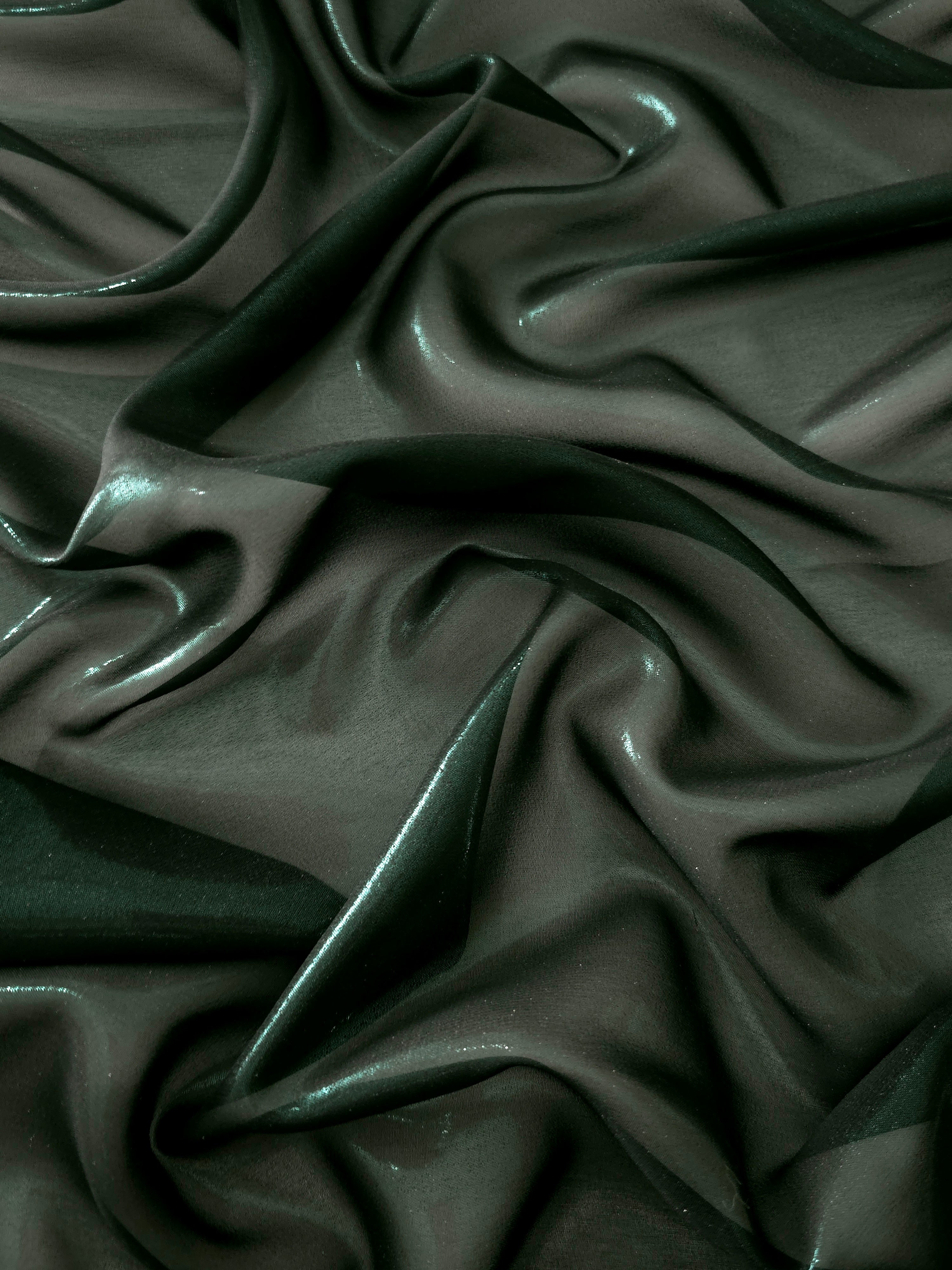 Deep forest surface detail view of liquid metallic shimmer chiffon fabric, highlighting fluid folds and reflective surface