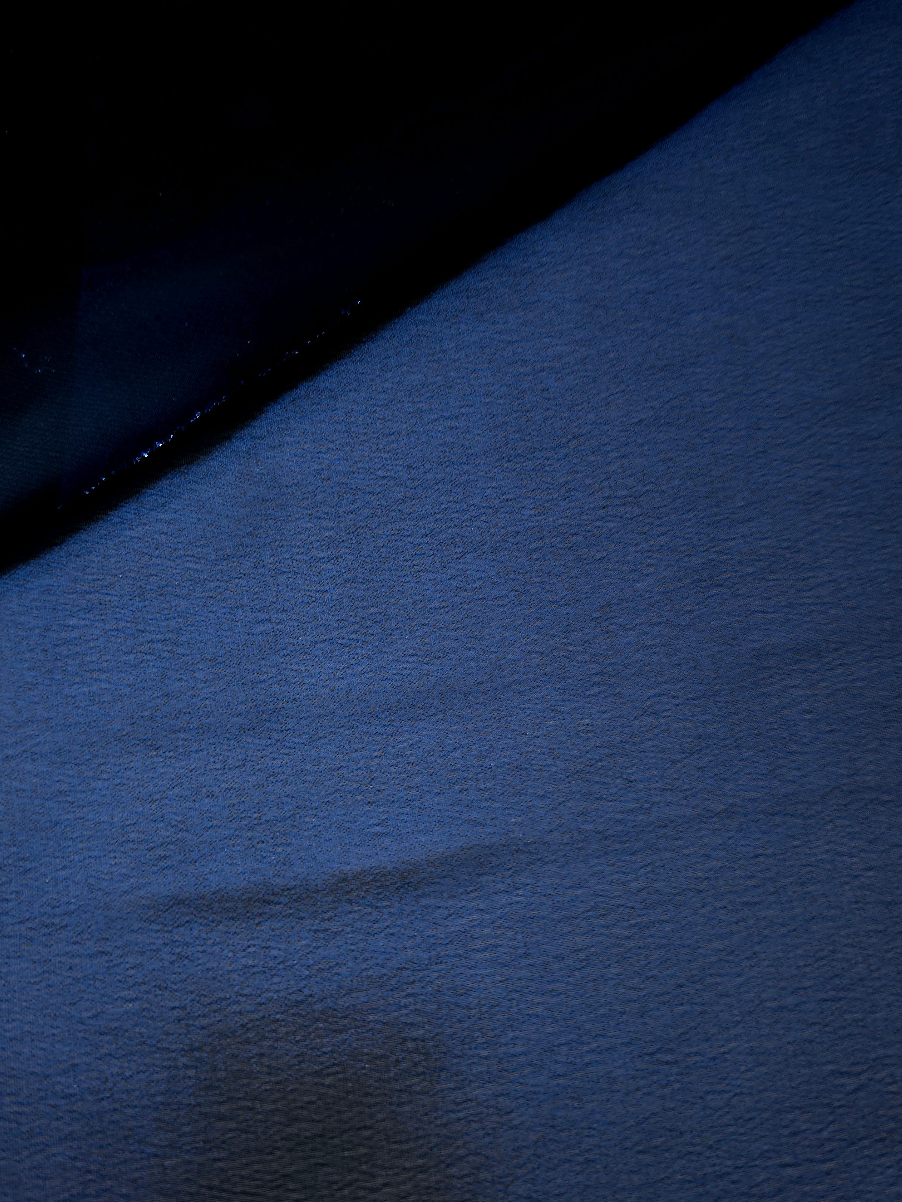 Deep indigo flowing folds of liquid metallic shimmer chiffon fabric, showing lightweight reflective fabric texture and drape