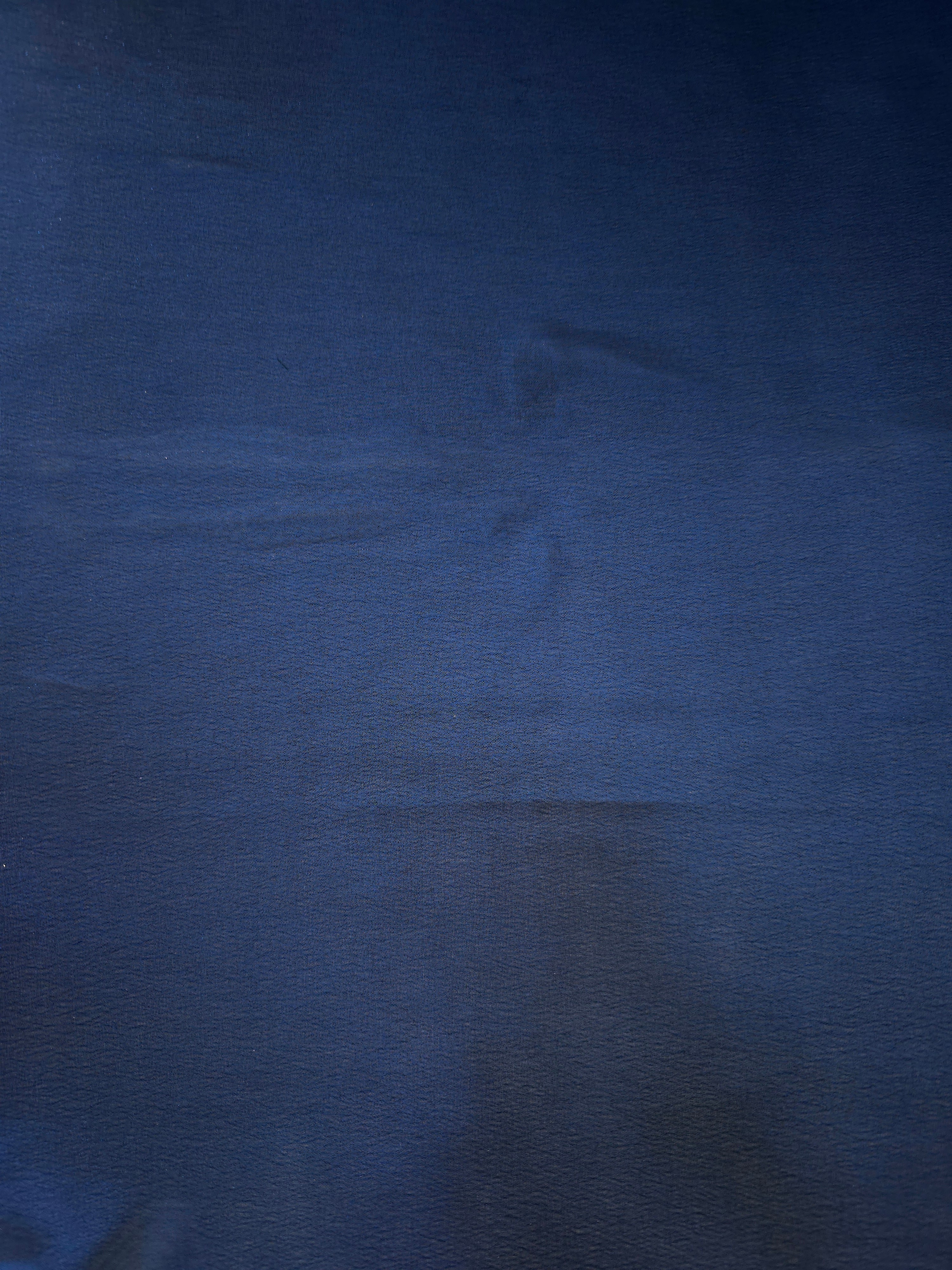 Deep indigo surface detail of liquid metallic shimmer chiffon fabric, showing lightweight reflective fabric texture and drape