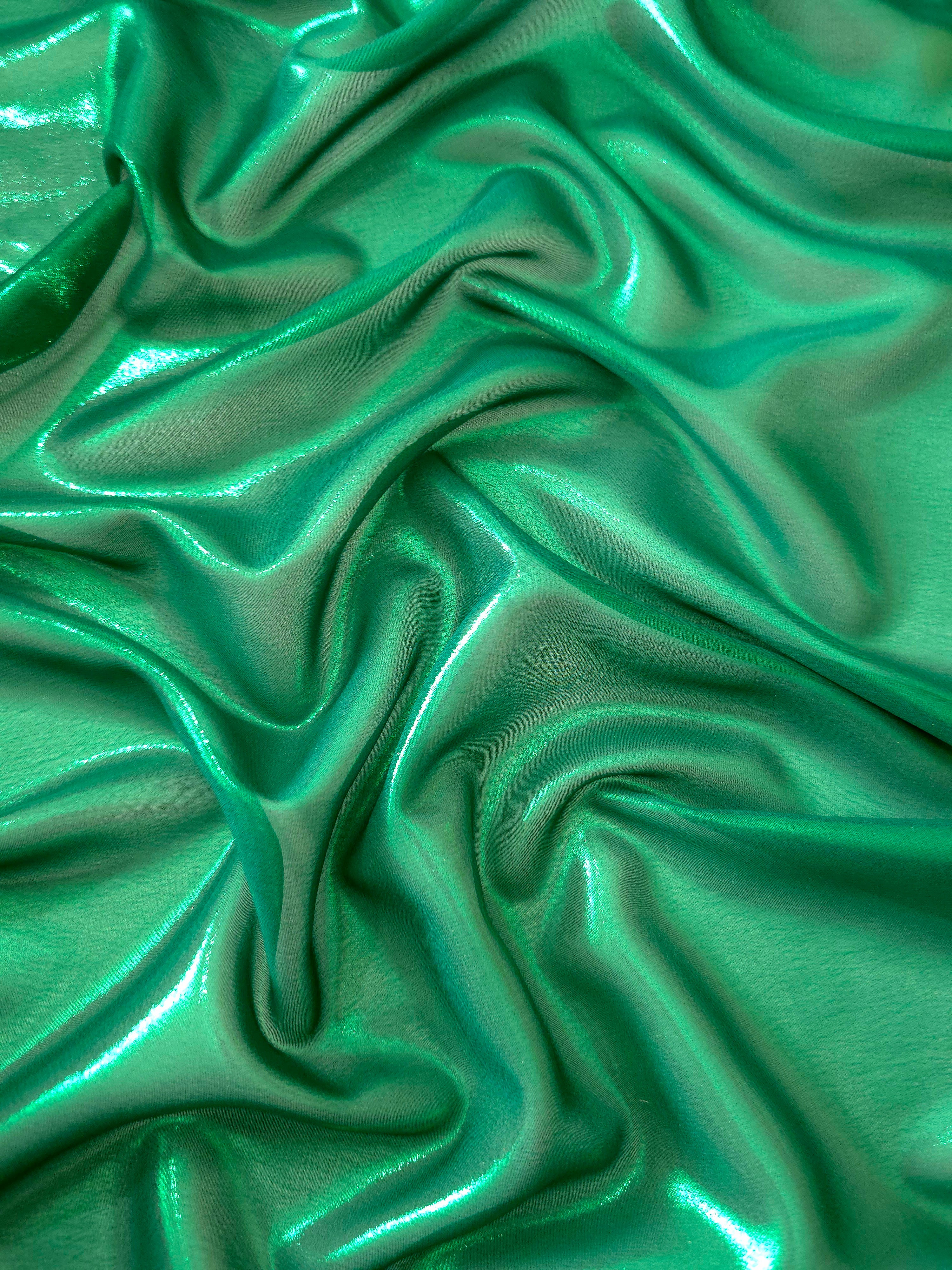 Emerald green surface detail view of liquid metallic shimmer chiffon fabric, highlighting fluid folds and reflective surface