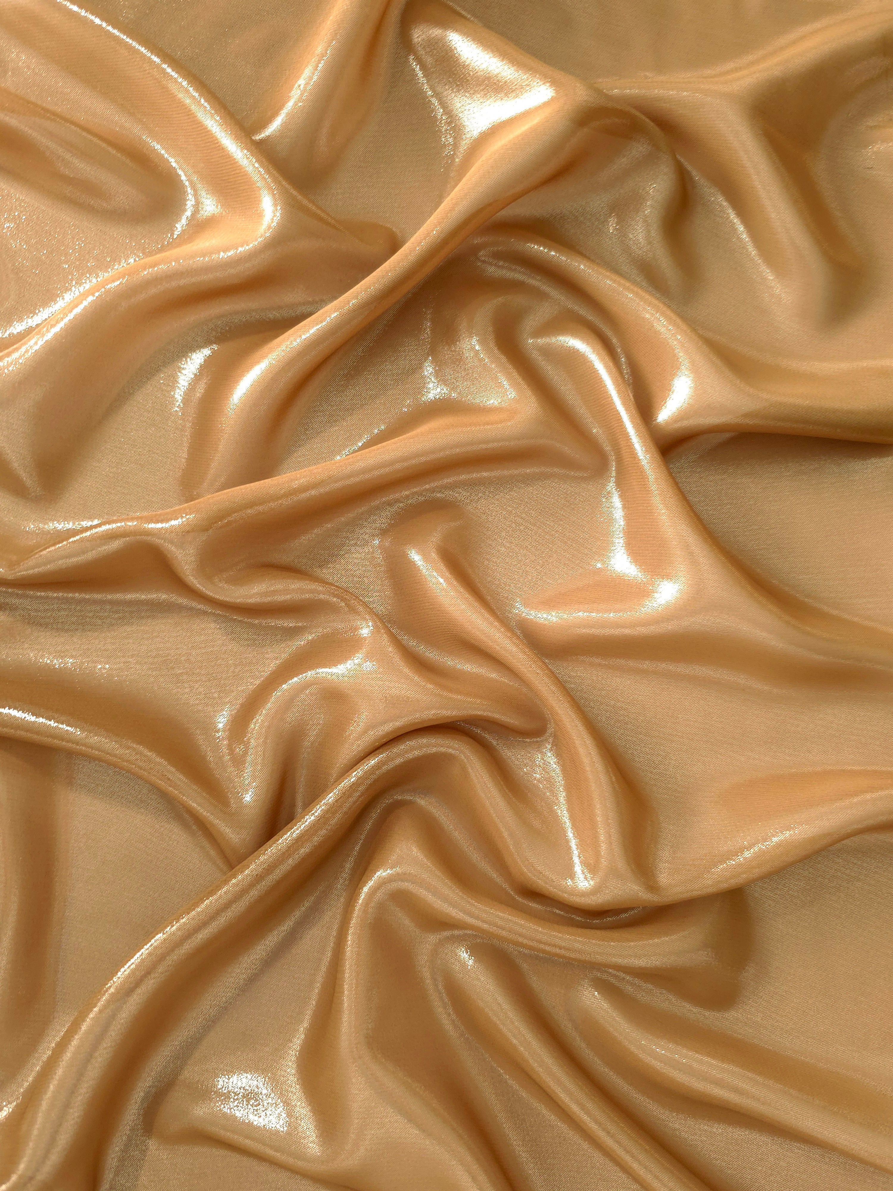 Golden sand surface detail view of liquid metallic shimmer chiffon fabric, highlighting fluid folds and reflective surface
