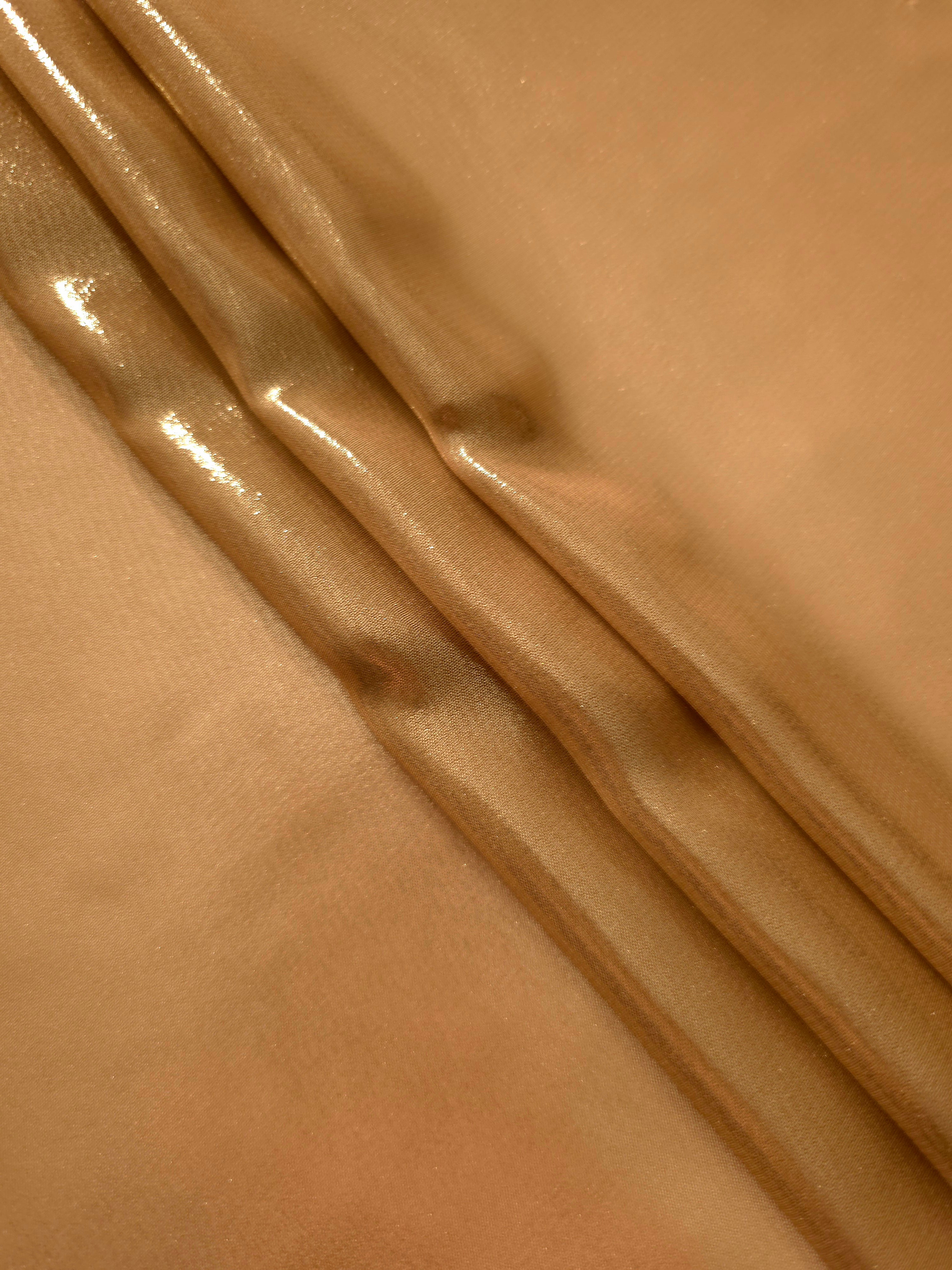 Golden tan flowing folds view of liquid metallic shimmer chiffon fabric, highlighting fluid folds and reflective surface
