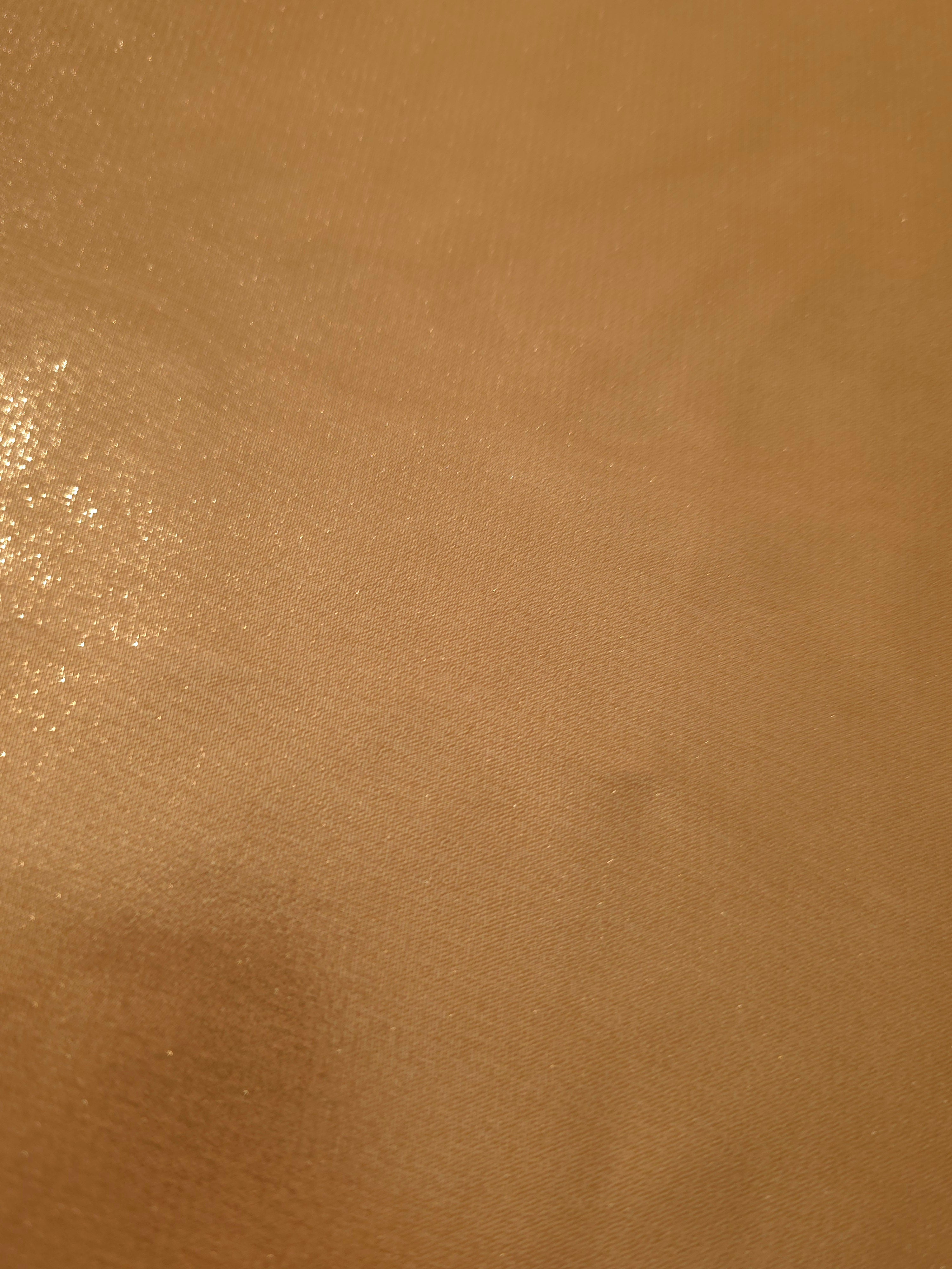 Golden tan fold detail view of liquid metallic shimmer chiffon fabric, highlighting fluid folds and reflective surface