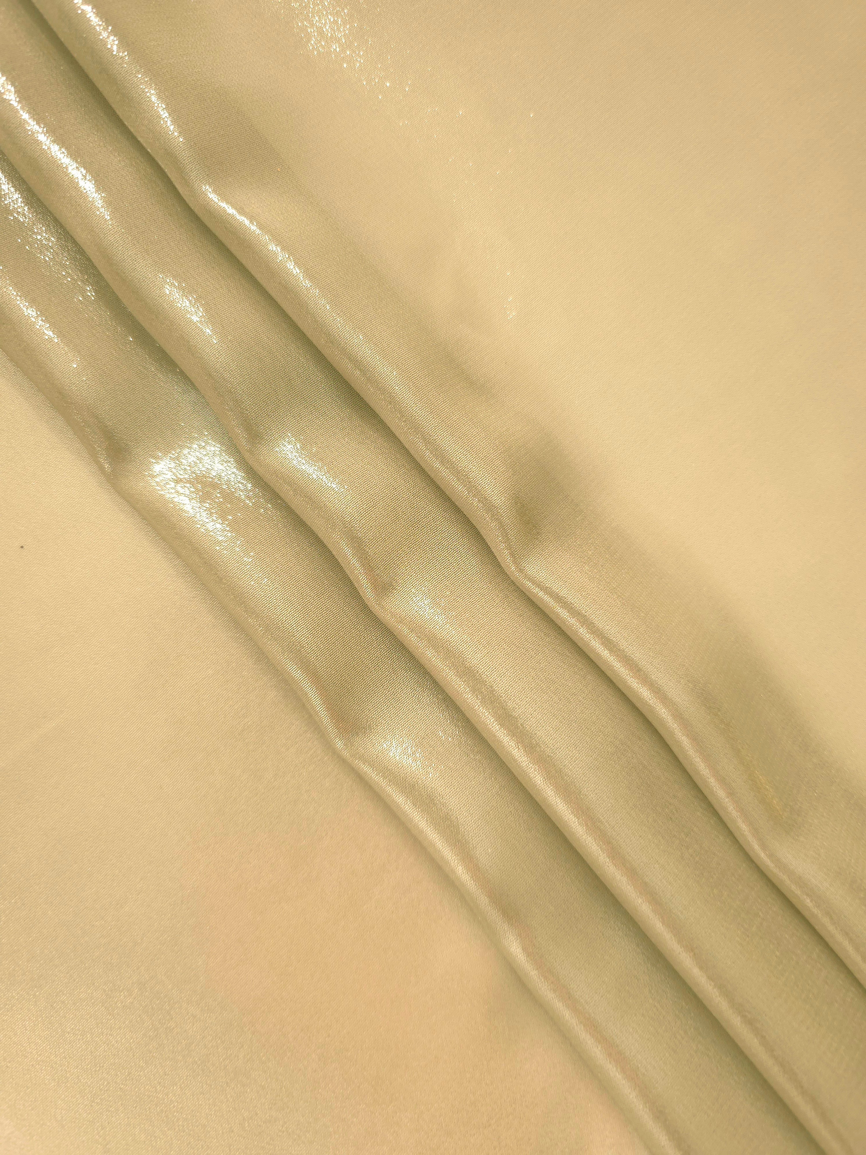 Pale gold flowing folds view of liquid metallic shimmer chiffon fabric, highlighting fluid folds and reflective surface