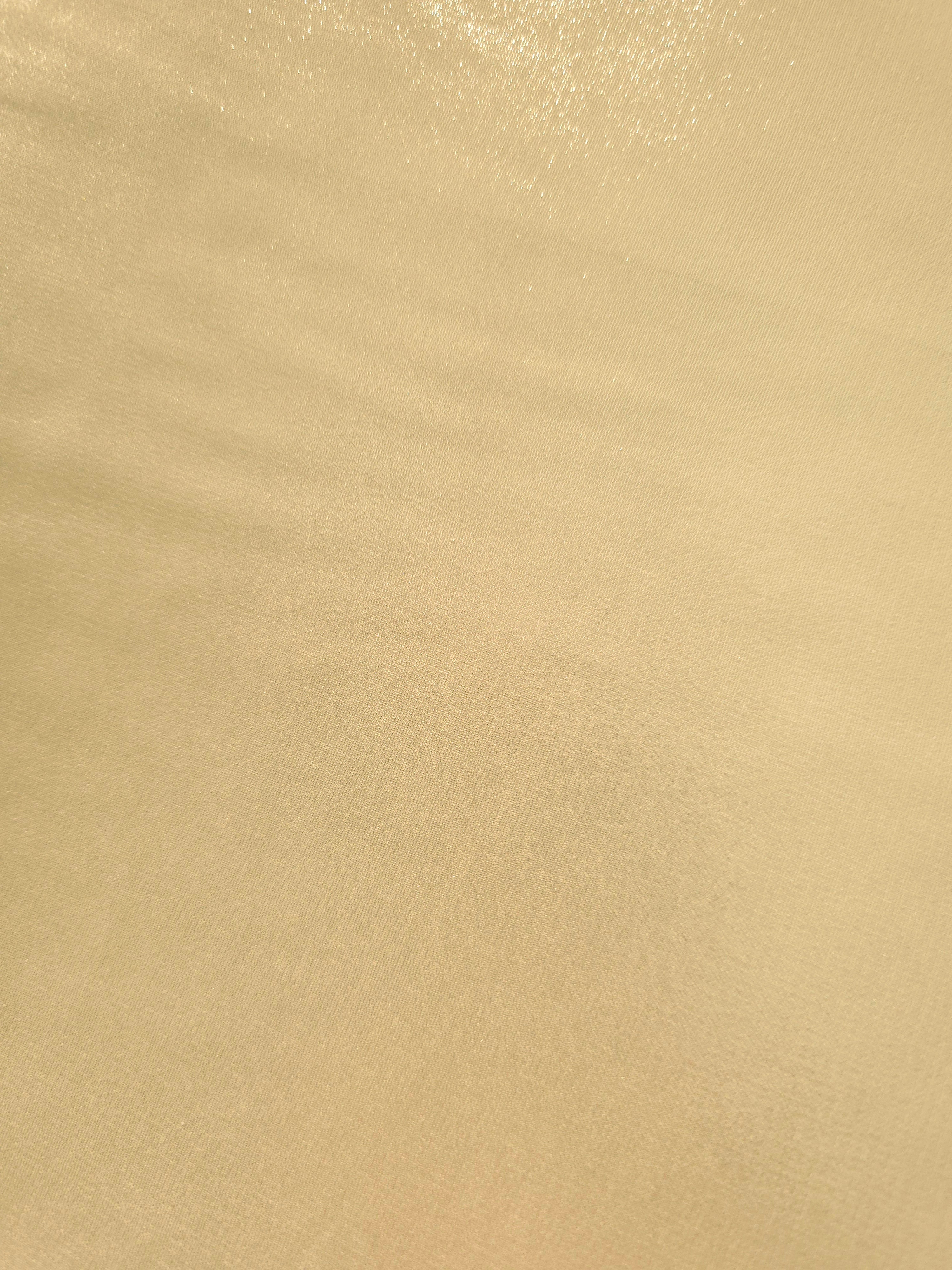 Pale gold fold detail view of liquid metallic shimmer chiffon fabric, highlighting fluid folds and reflective surface