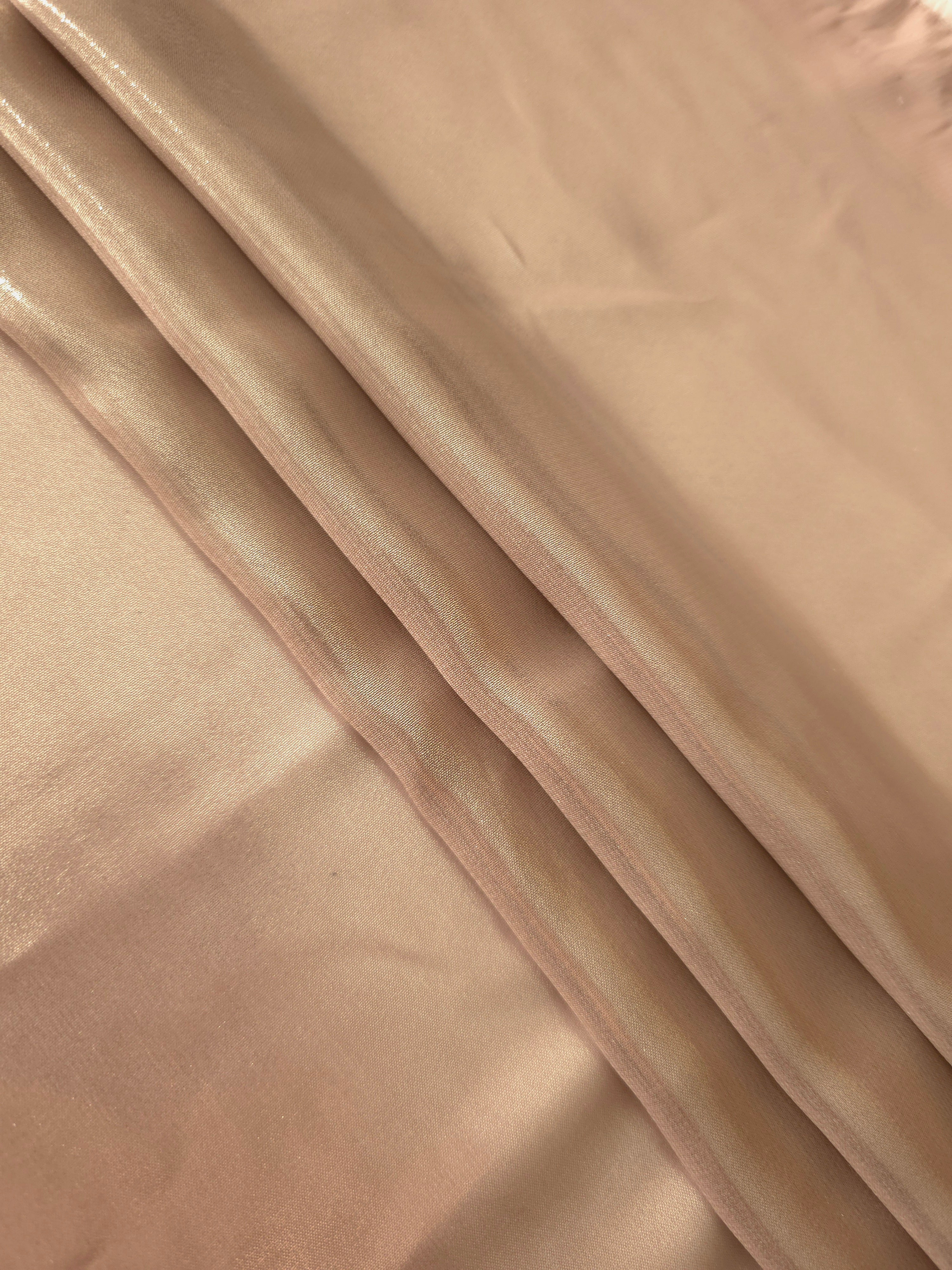 Peach champagne flowing folds view of liquid metallic shimmer chiffon fabric, highlighting fluid folds and reflective surface