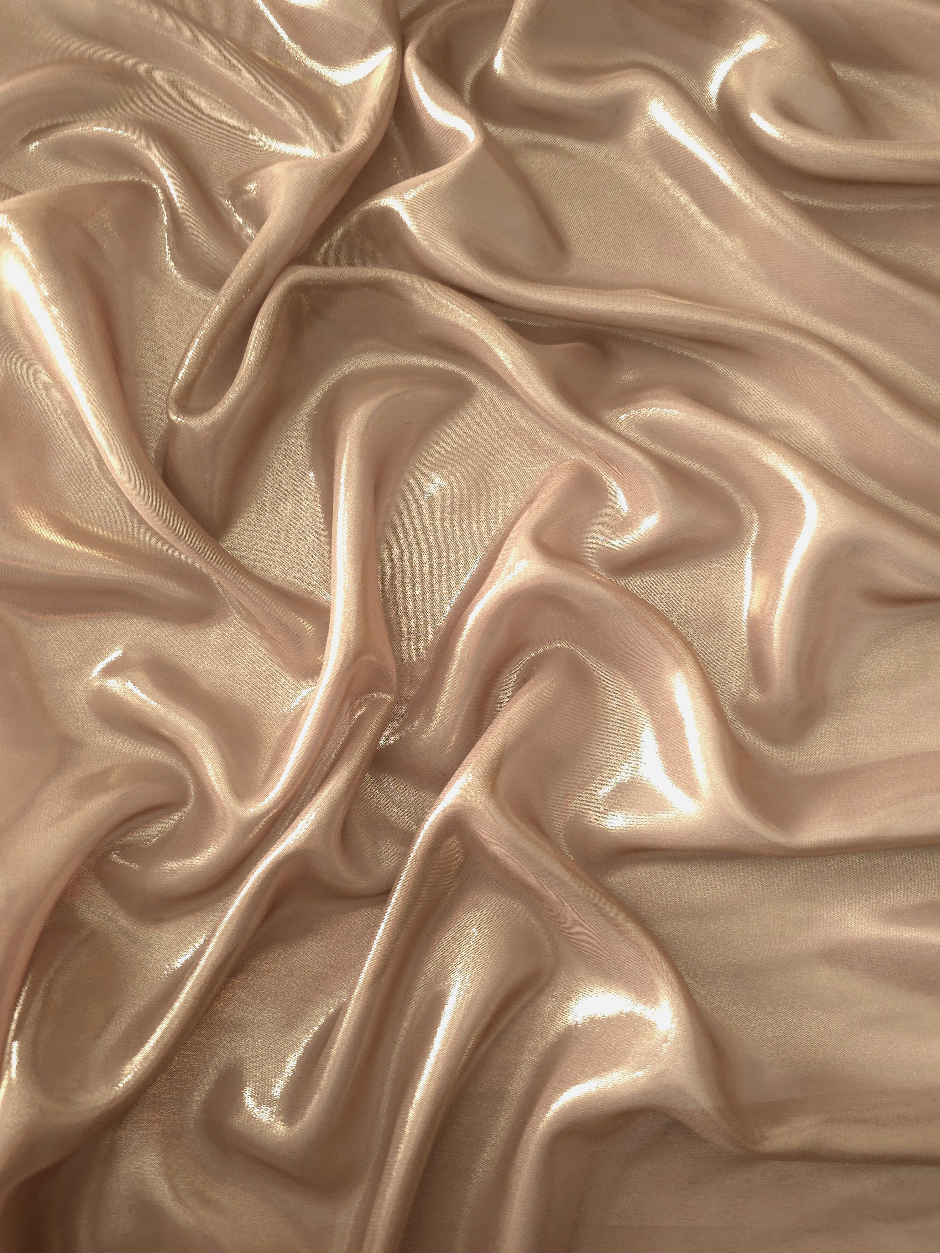Peach champagne surface detail view of liquid metallic shimmer chiffon fabric, highlighting fluid folds and reflective surface