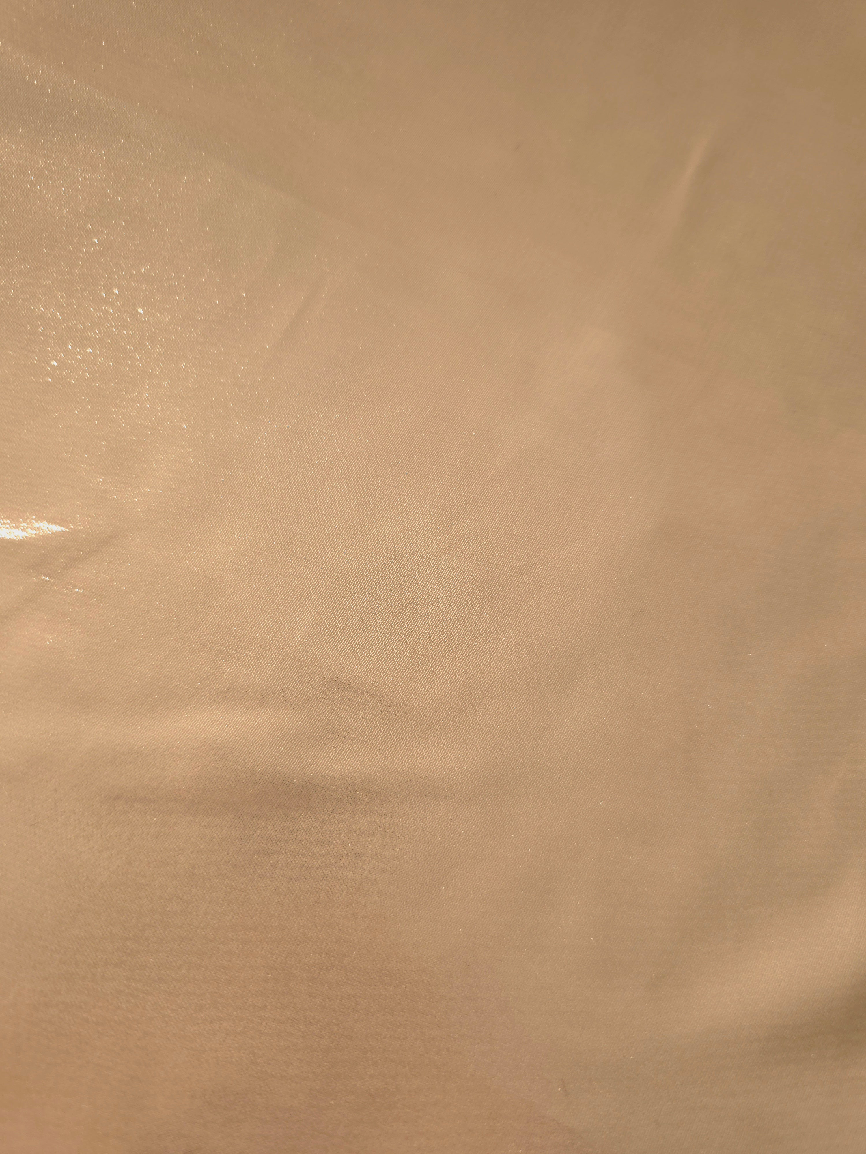 Soft taupe fold detail of liquid metallic shimmer chiffon fabric, showing lightweight reflective fabric texture and drape