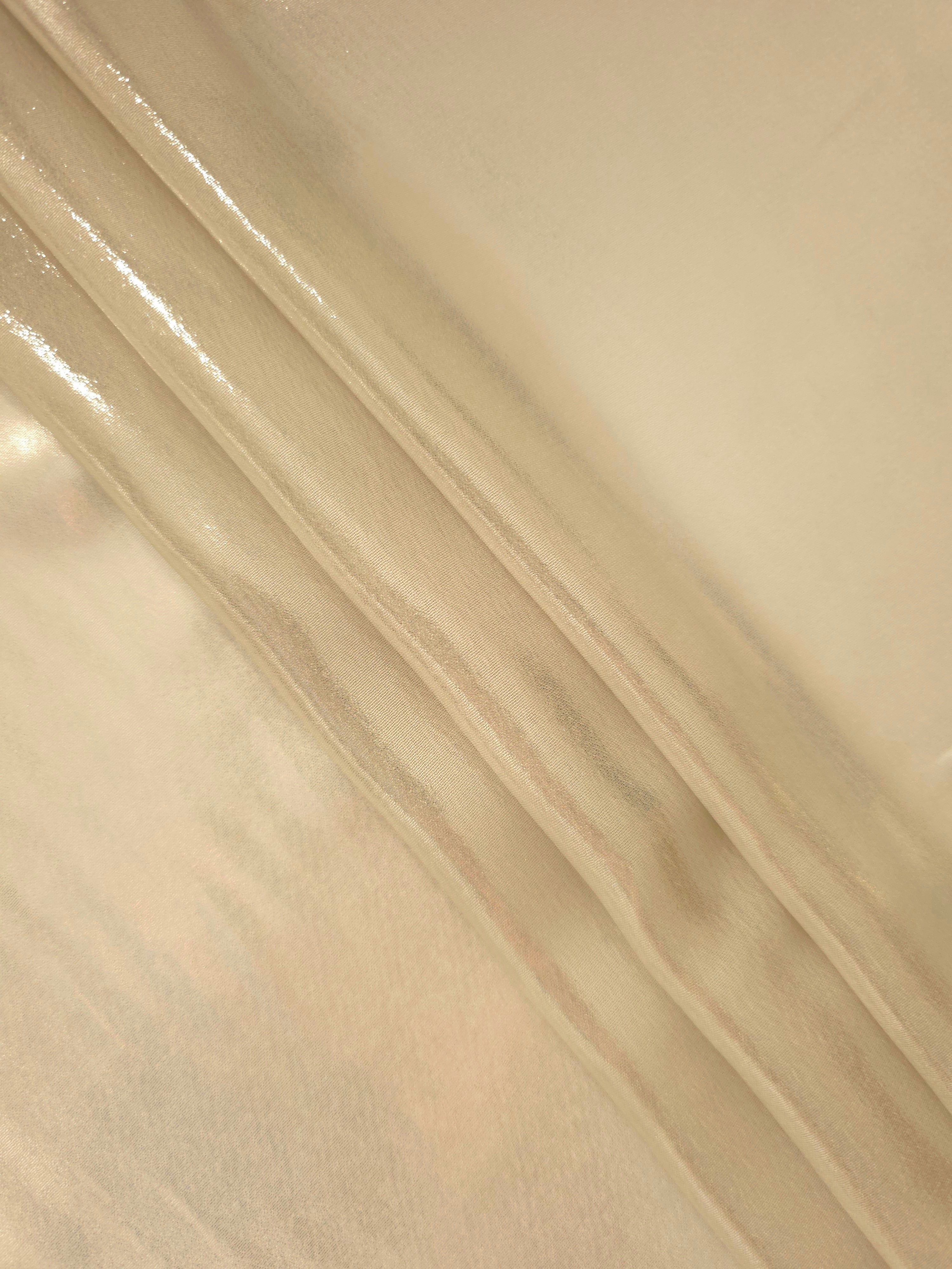 Warm ivory flowing folds of liquid metallic shimmer chiffon fabric, showing lightweight reflective fabric texture and drape