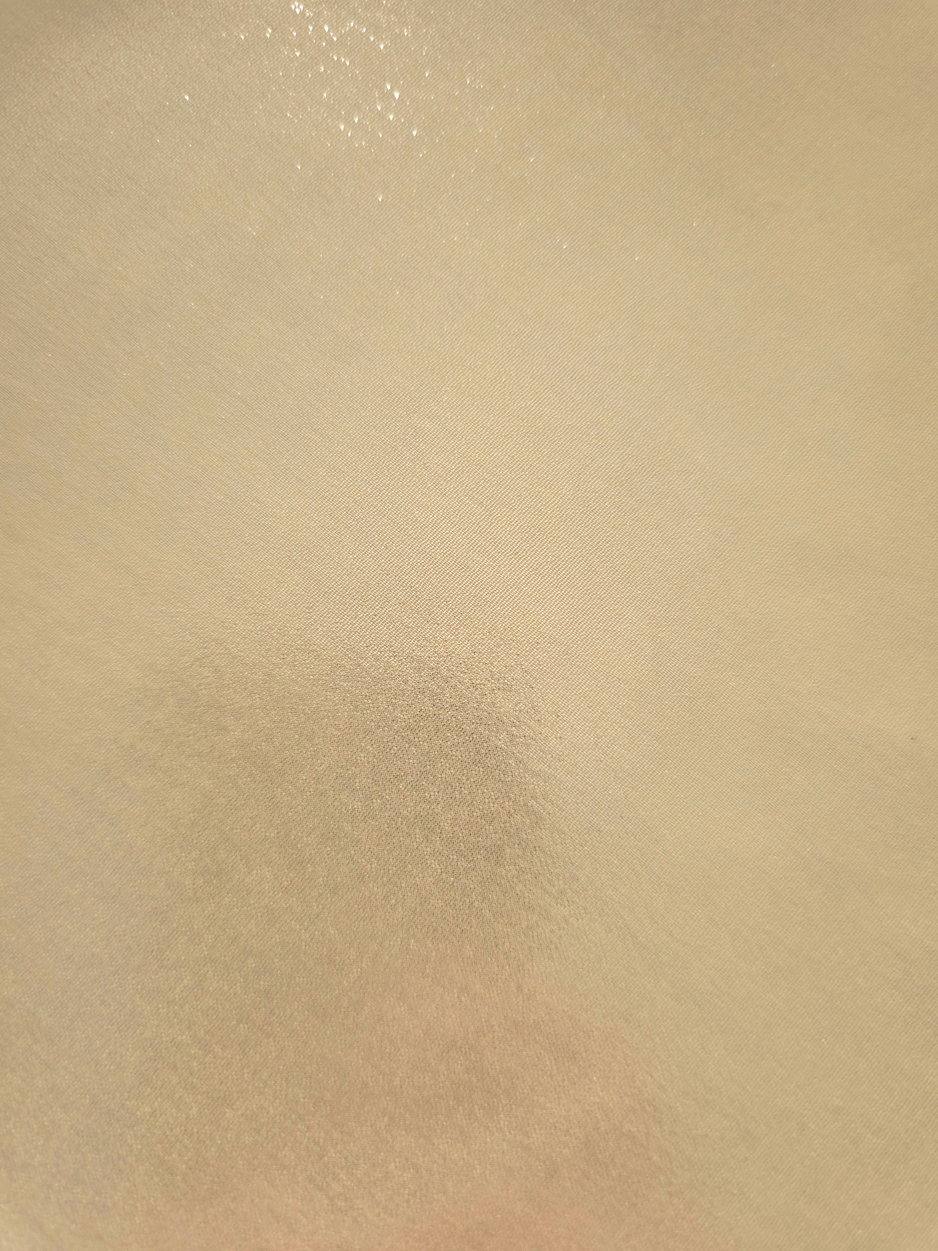 Warm ivory fold detail of liquid metallic shimmer chiffon fabric, showing lightweight reflective fabric texture and drape