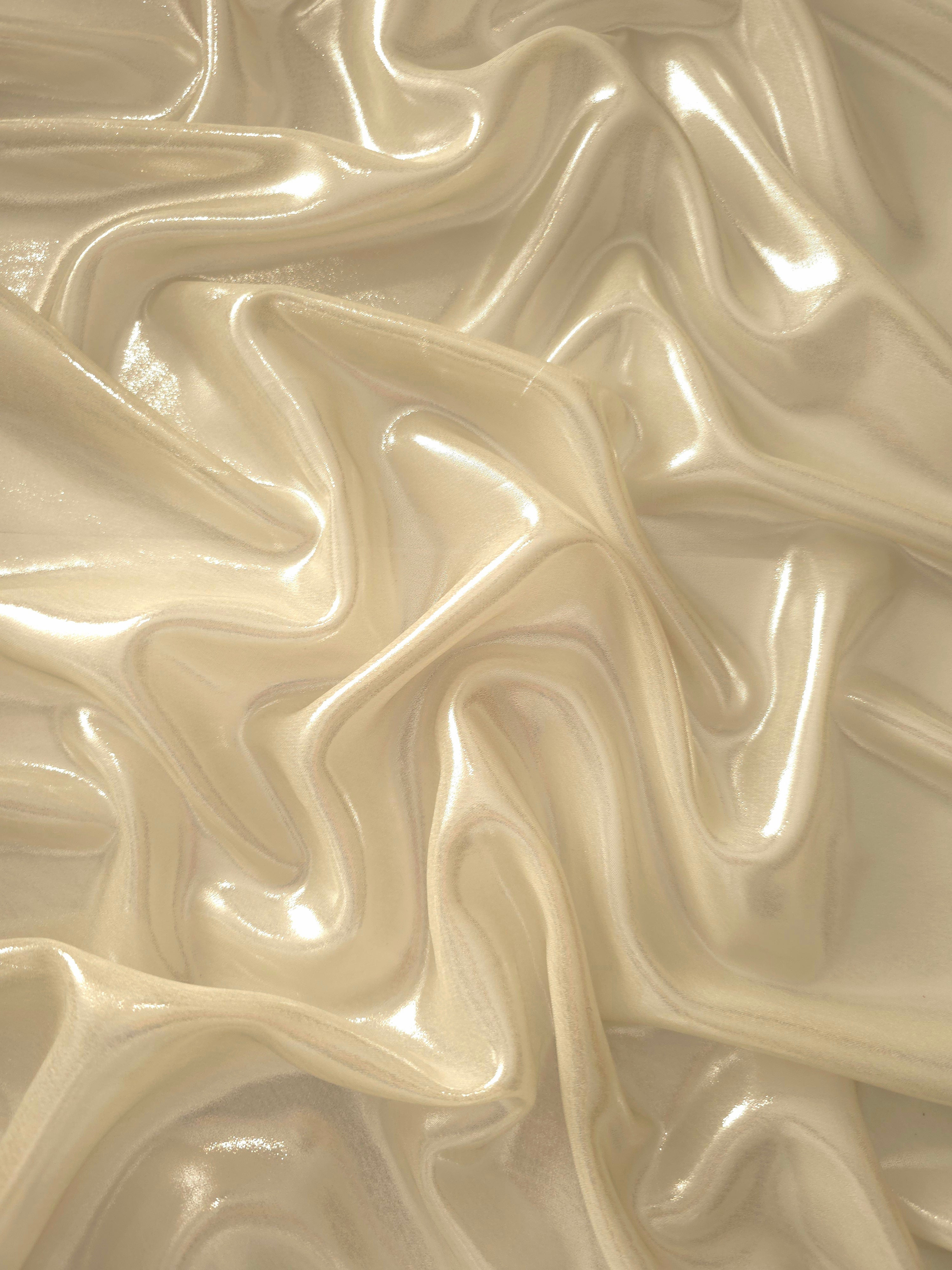 Warm ivory surface detail of liquid metallic shimmer chiffon fabric, showing lightweight reflective fabric texture and drape
