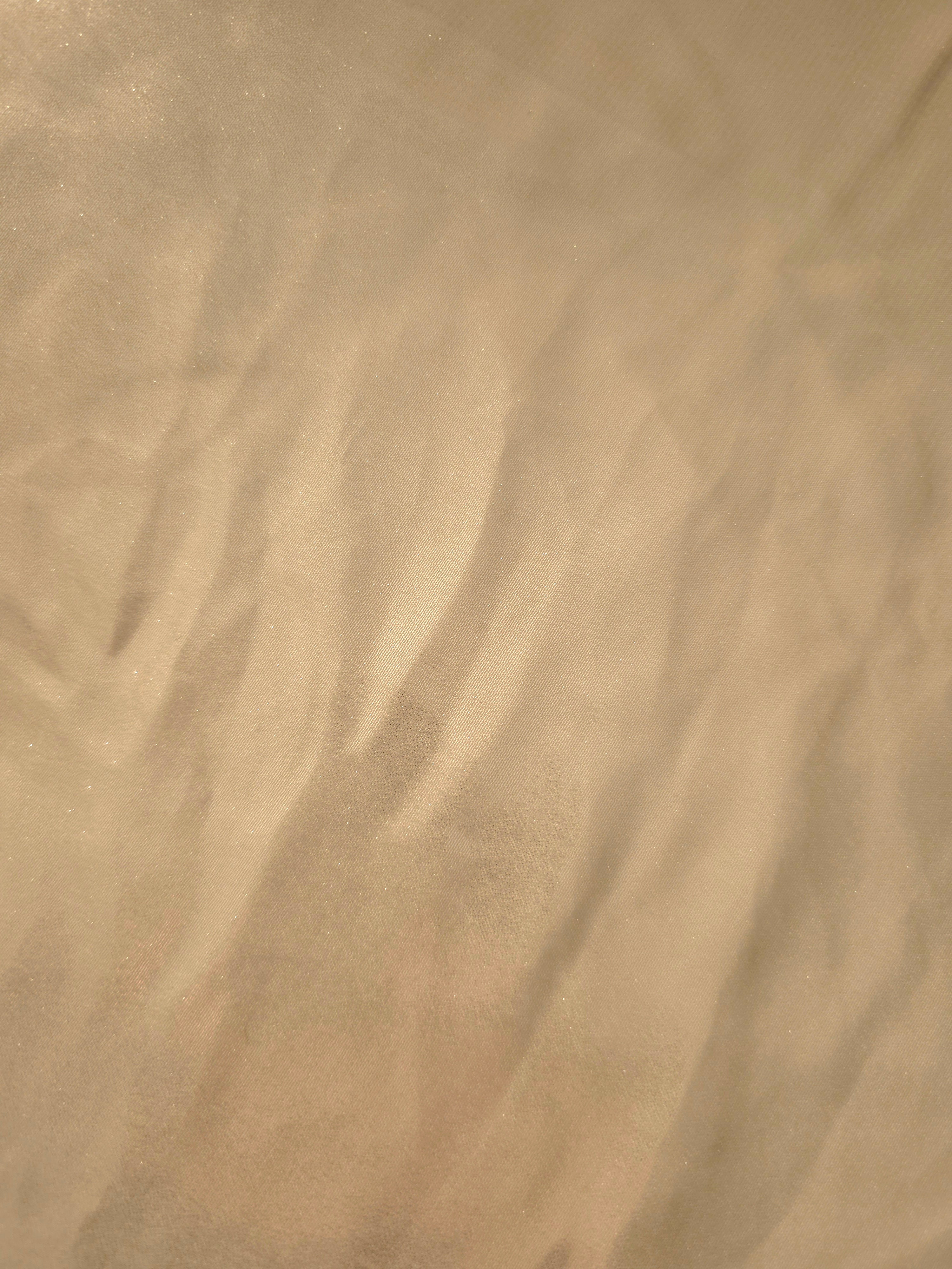 Warm sand fold detail of liquid metallic shimmer chiffon fabric, showing lightweight reflective fabric texture and drape