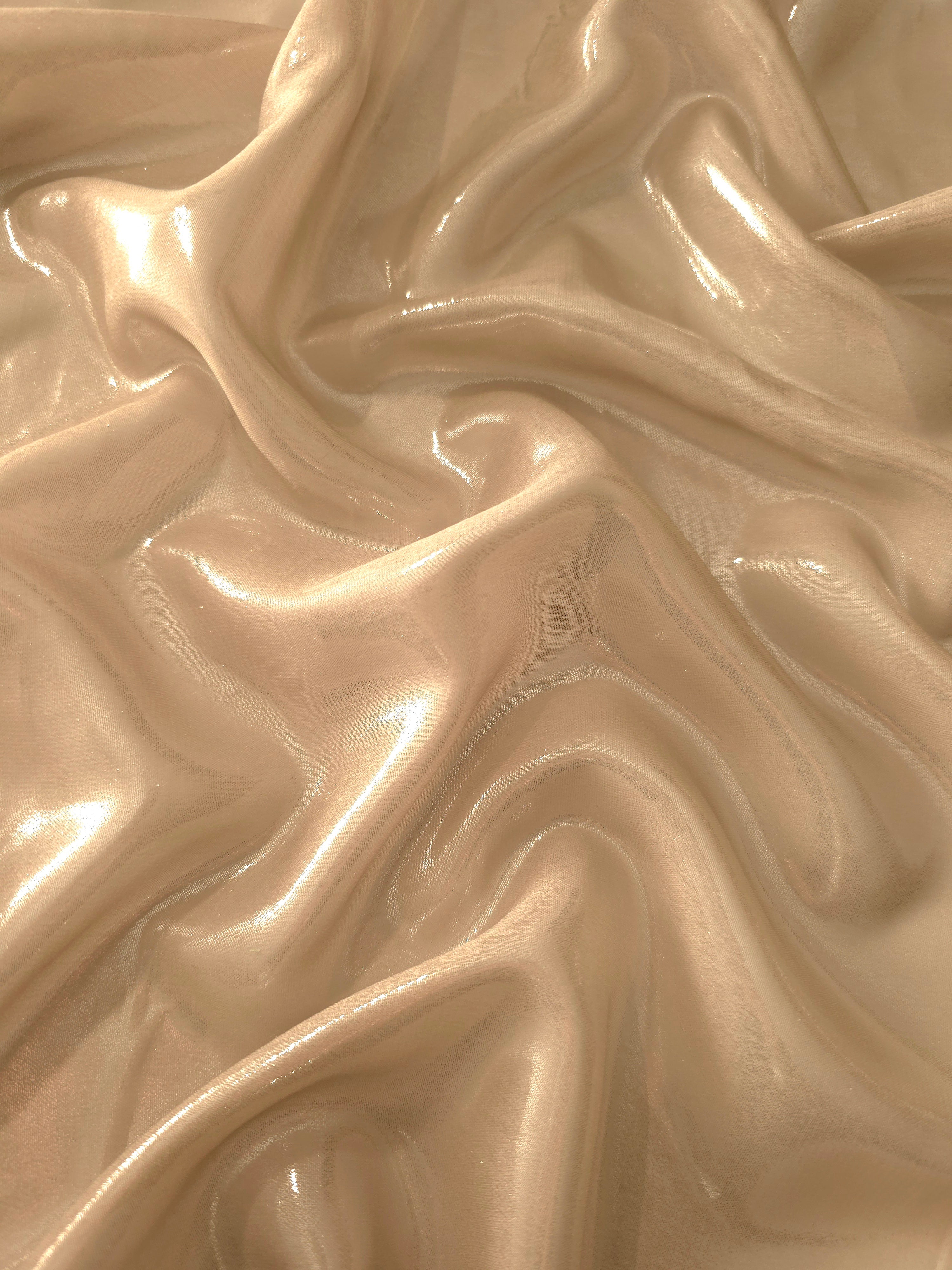 Warm sand surface detail of liquid metallic shimmer chiffon fabric, showing lightweight reflective fabric texture and drape