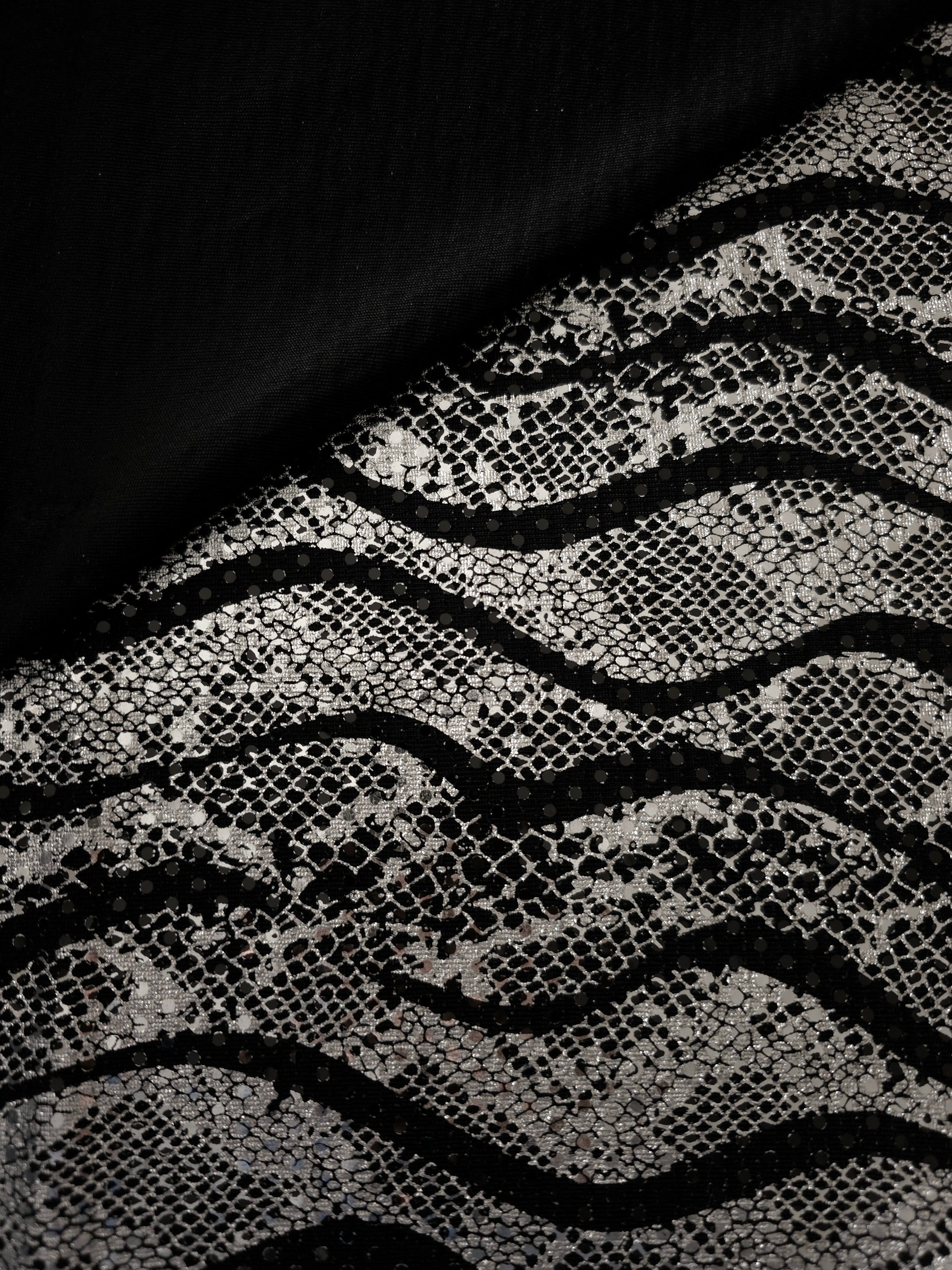 Close fold view of Silver Gray Wavy Python foil sequin mesh, showing how the reflective pattern gathers across black tulle for occasion skirts, bodice panels and stagewear.