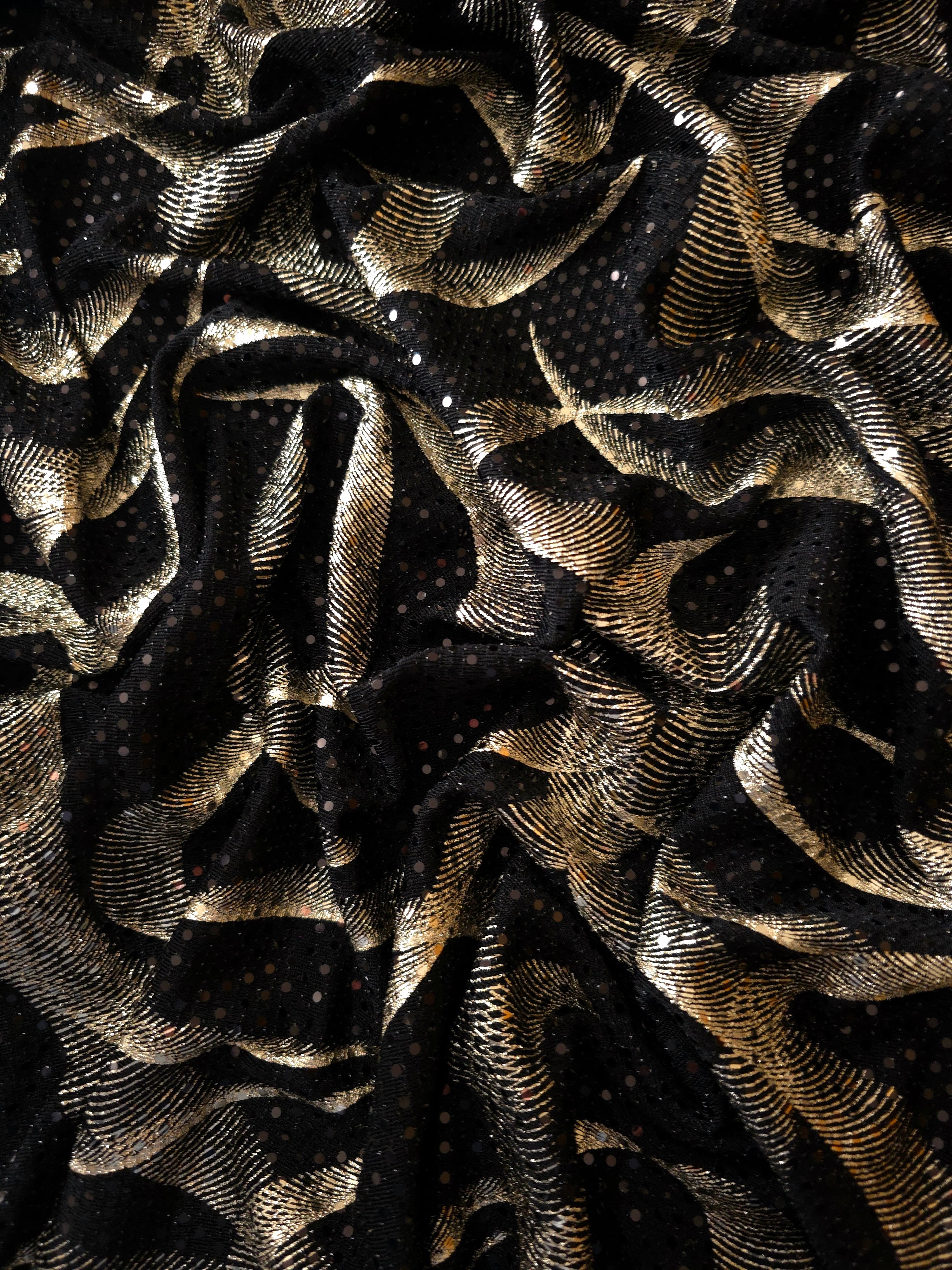 Flowing drape of Soft Gold Abstract Ribbon foil sequin fabric over a black mesh base, highlighting shimmer and fluid fall for prom dresses, cocktail looks and statement overlays.