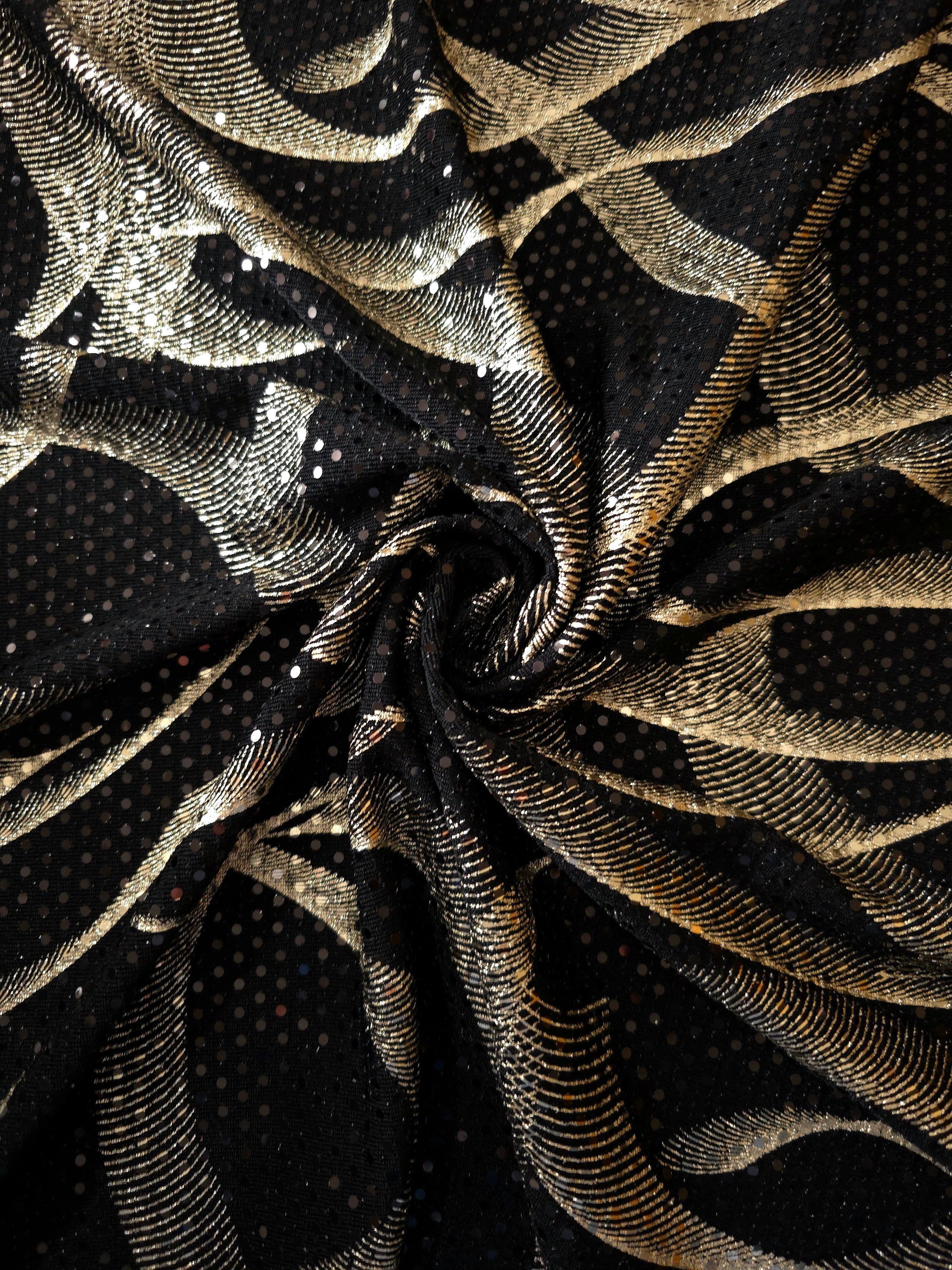 Twisted drape of Soft Gold Abstract Ribbon metallic foil sequin fabric, emphasizing light-catching movement over black tulle for formal dresses, cape details and performance costumes.