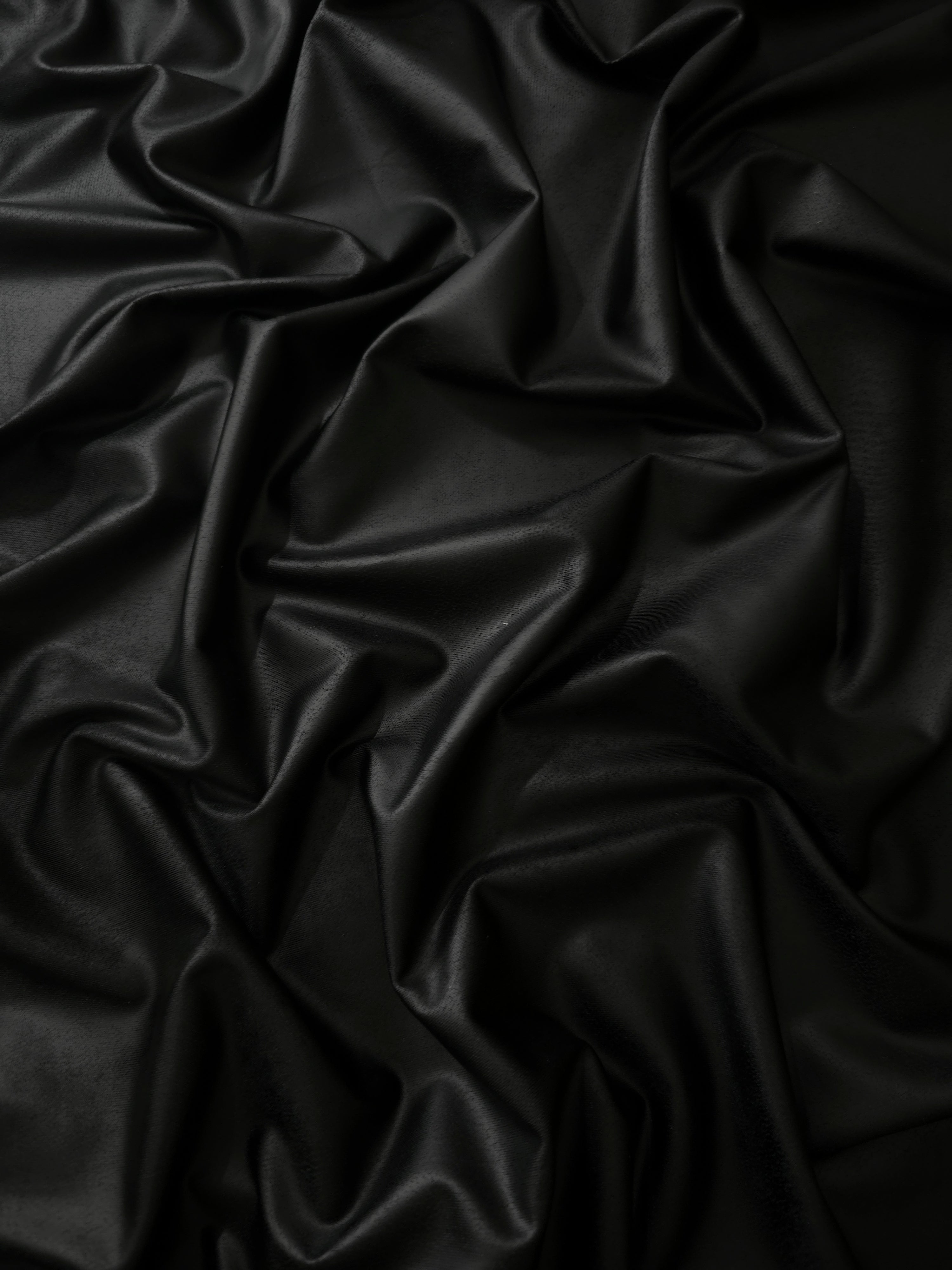Loose drape of black soft faux leather stretch fabric showing flexible movement for bodycon dresses, pencil skirts and sleek trousers.