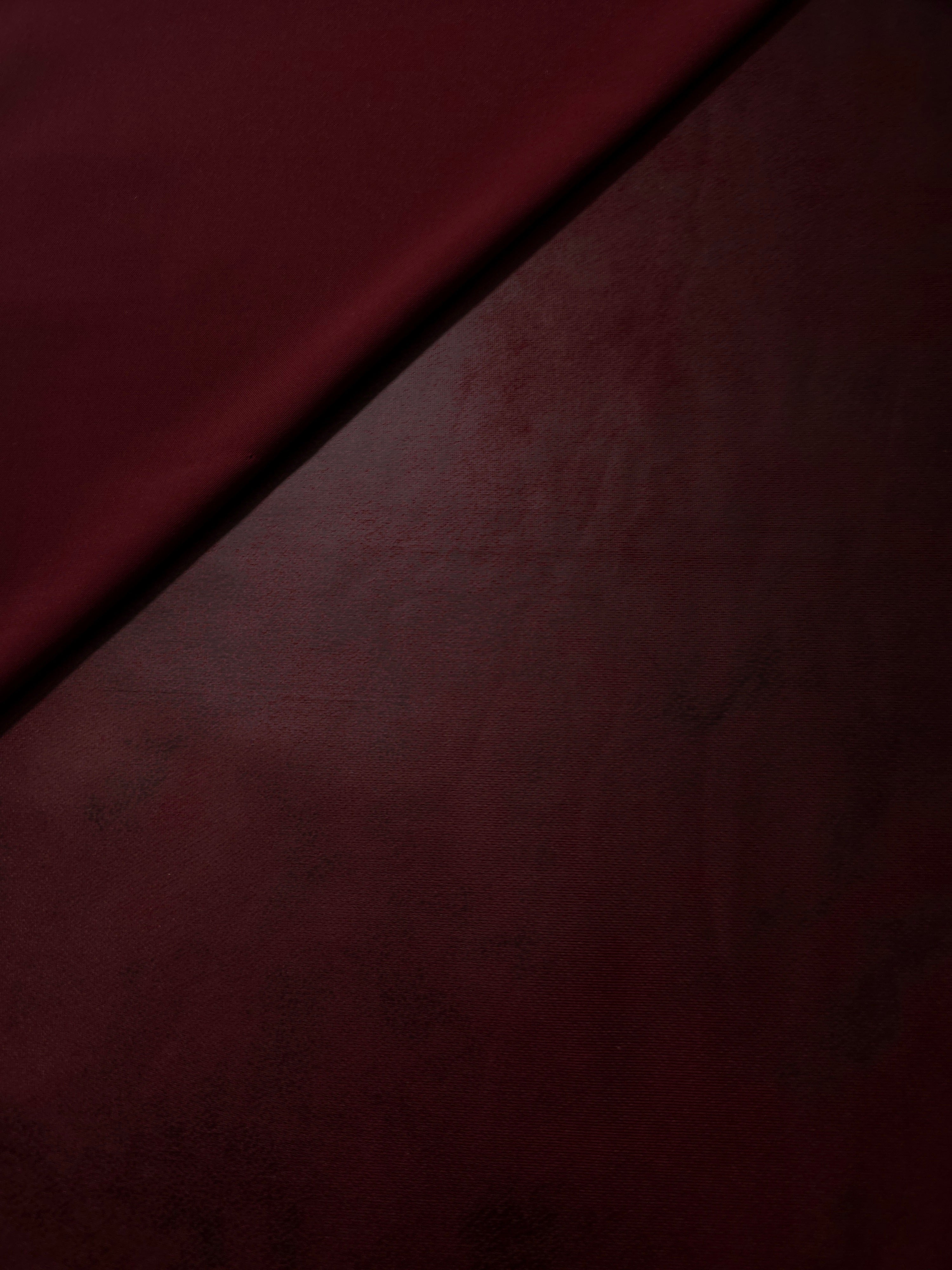 Front and backing sides of burgundy red faux leather stretch fabric shown for jackets, structured tops and fashion construction.