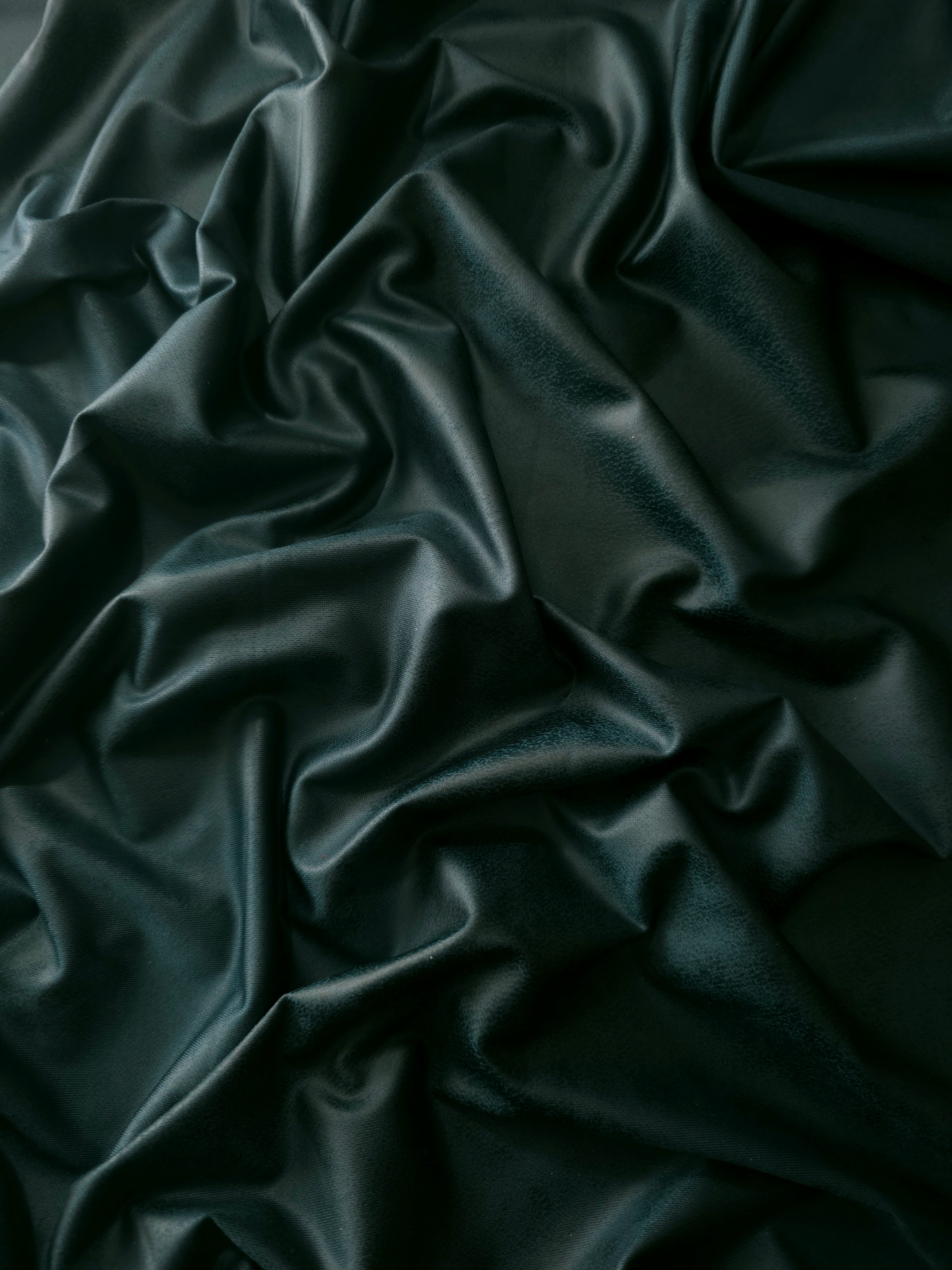 Loose folds of deep forest green soft faux leather stretch fabric demonstrating drape for bodycon dresses and modern skirts.