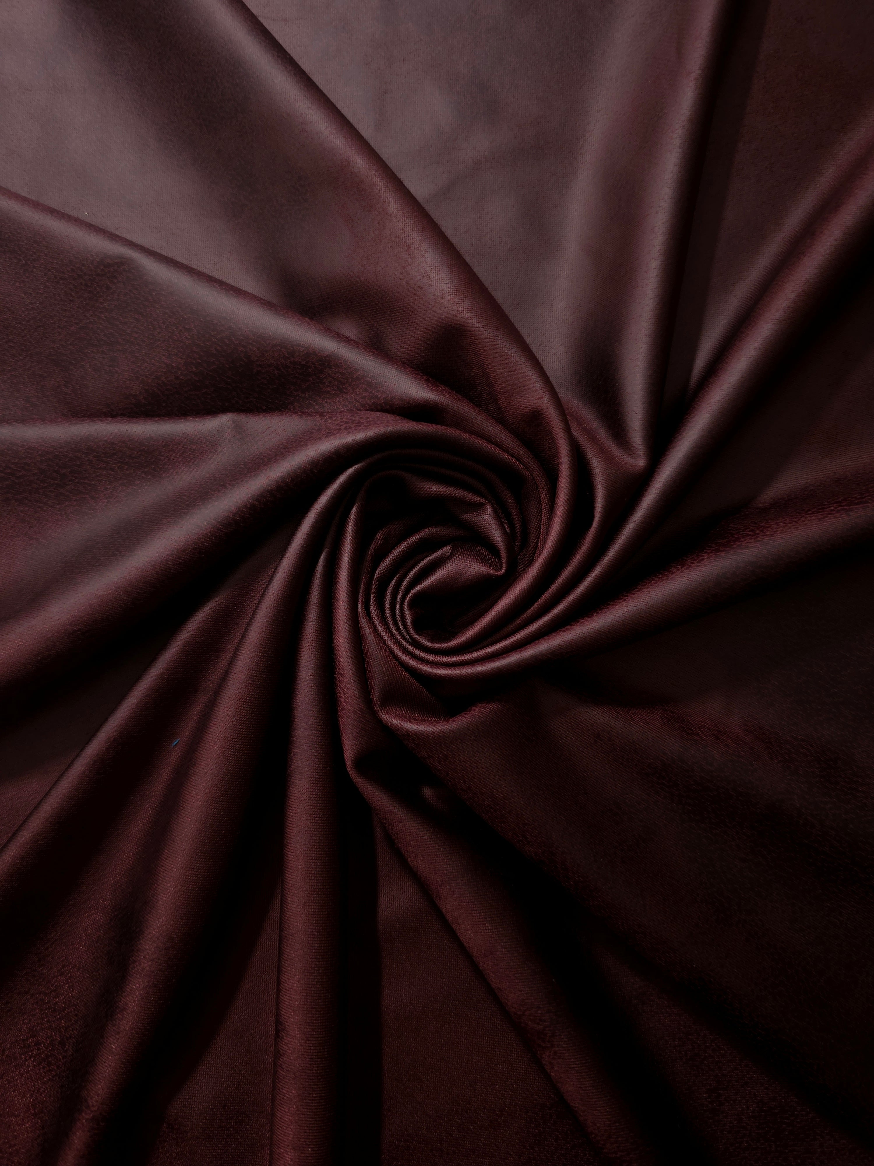 Spiral arrangement of deep plum leather-effect stretch fabric emphasizing supple folds for statement dresses and performance wear.
