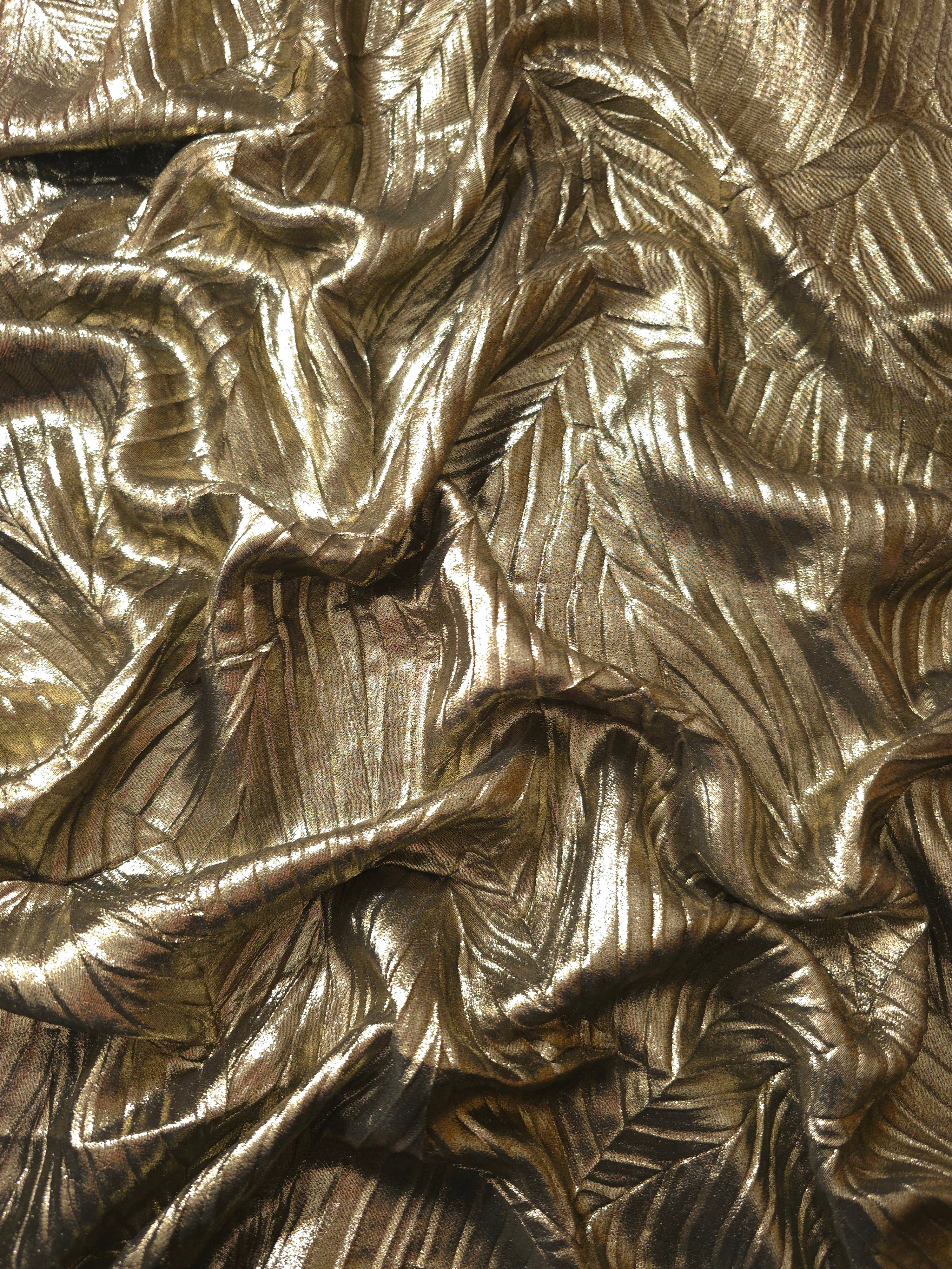 Flowing drape of Antique Gold leaf-pattern plissé shimmer fabric, showing sculpted leaf-like pleats and light-catching movement for evening gowns and flowing maxi skirts.