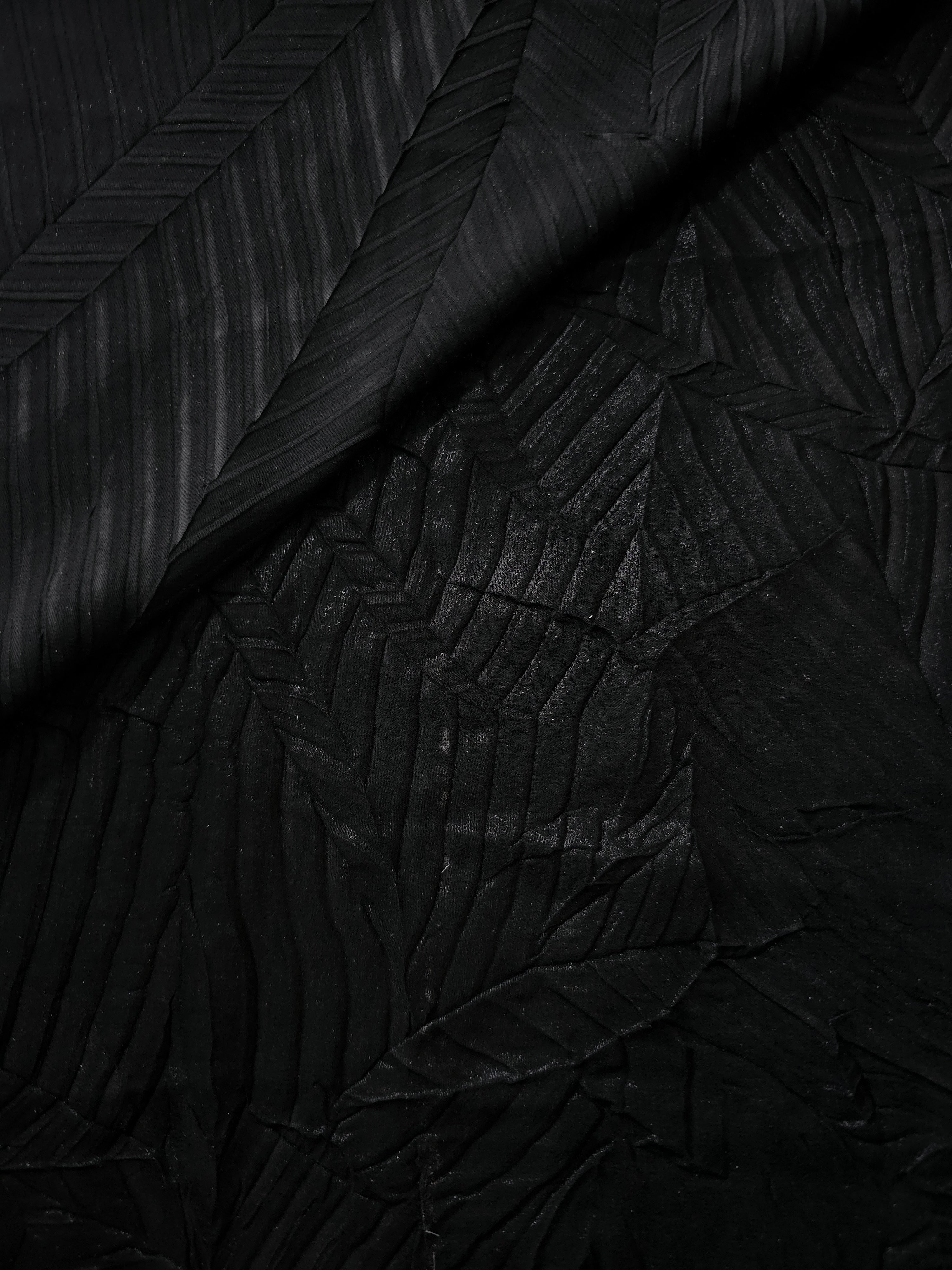 Draped movement in Obsidian Black leaf-pattern plissé shimmer fabric highlights the reflective pleat structure for party dresses and fluid statement separates.