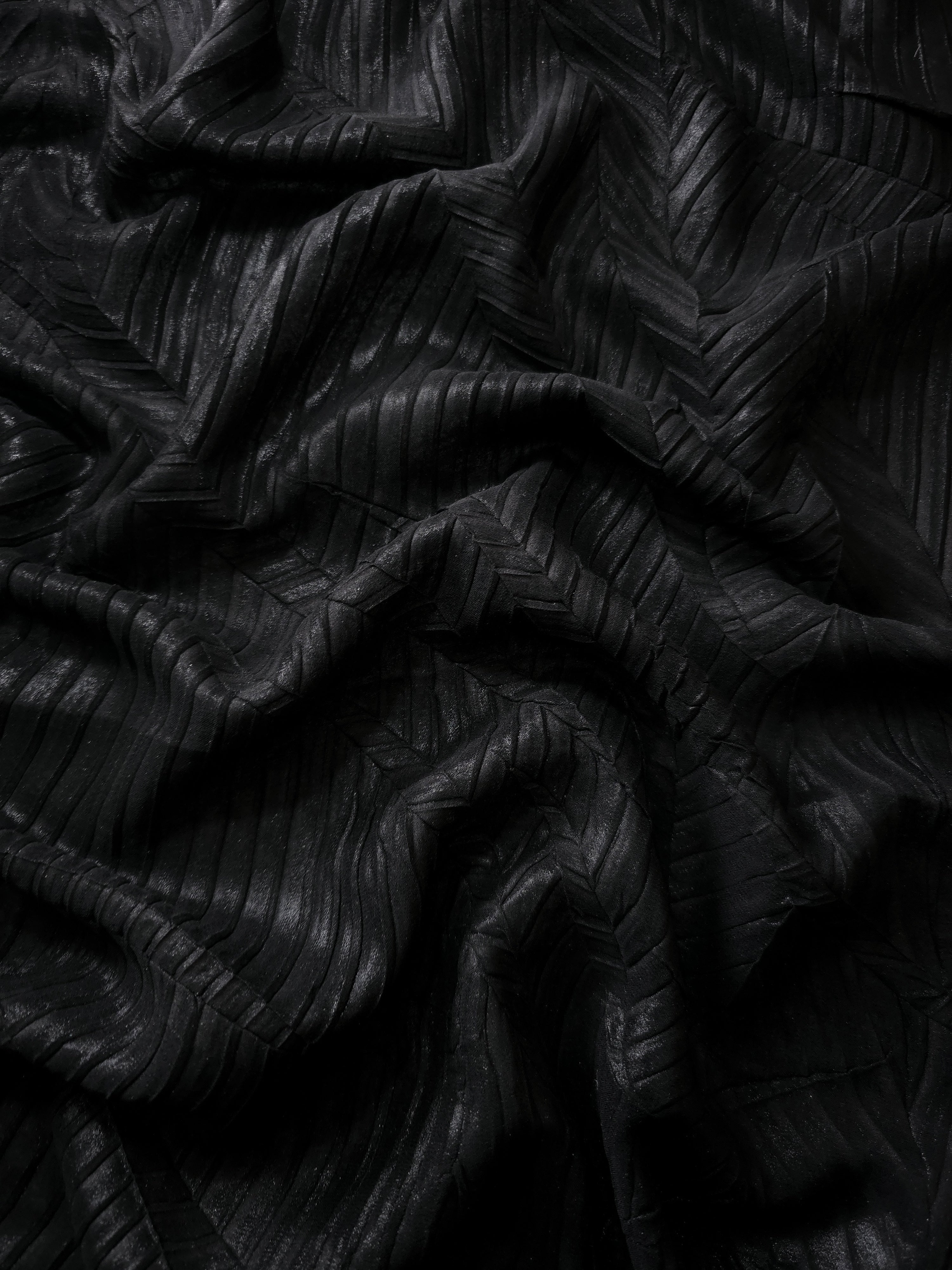 Folded Obsidian Black leaf-pattern plissé shimmer fabric, revealing layered sculpted leaf-like pleats and changing highlights for pleated skirts and structured party pieces.