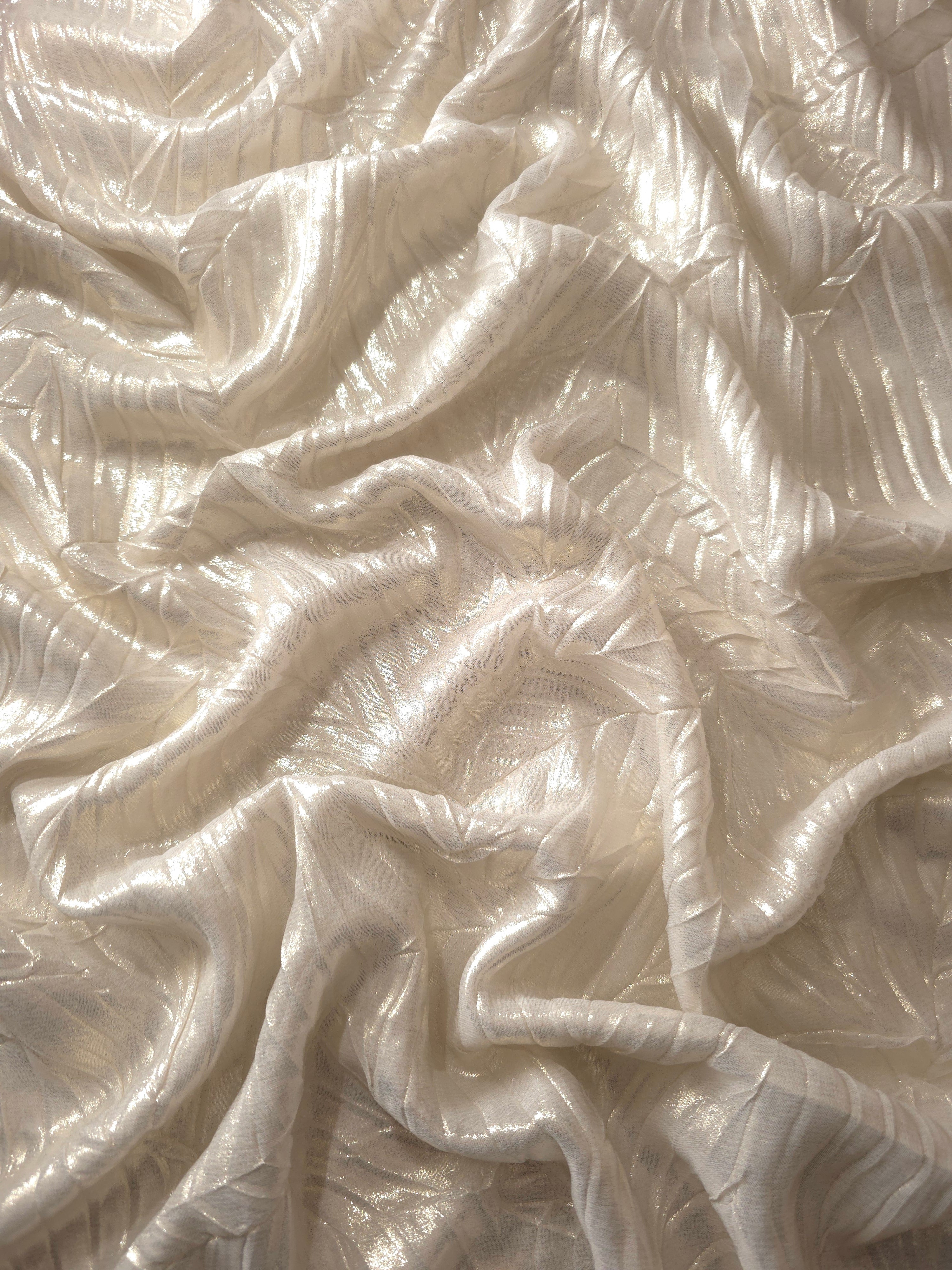 Flowing drape of Pearl Ivory leaf-pattern plissé shimmer fabric, showing sculpted leaf-like pleats and light-catching movement for evening gowns and flowing maxi skirts.