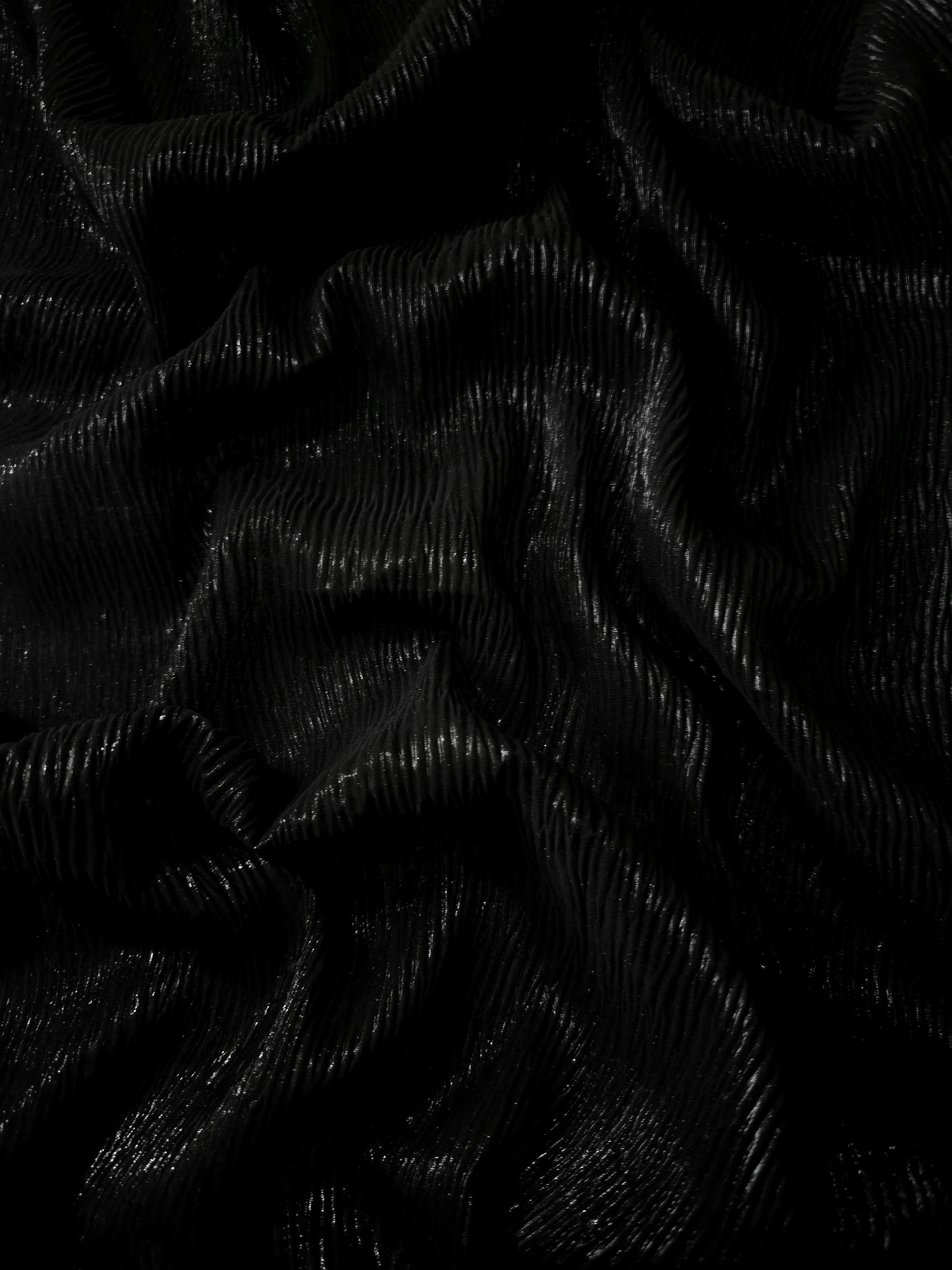 Flowing drape of Jet Black fine mini-plissé shimmer fabric, showing narrow micro-pleated texture and light-catching movement for evening gowns and flowing maxi skirts.