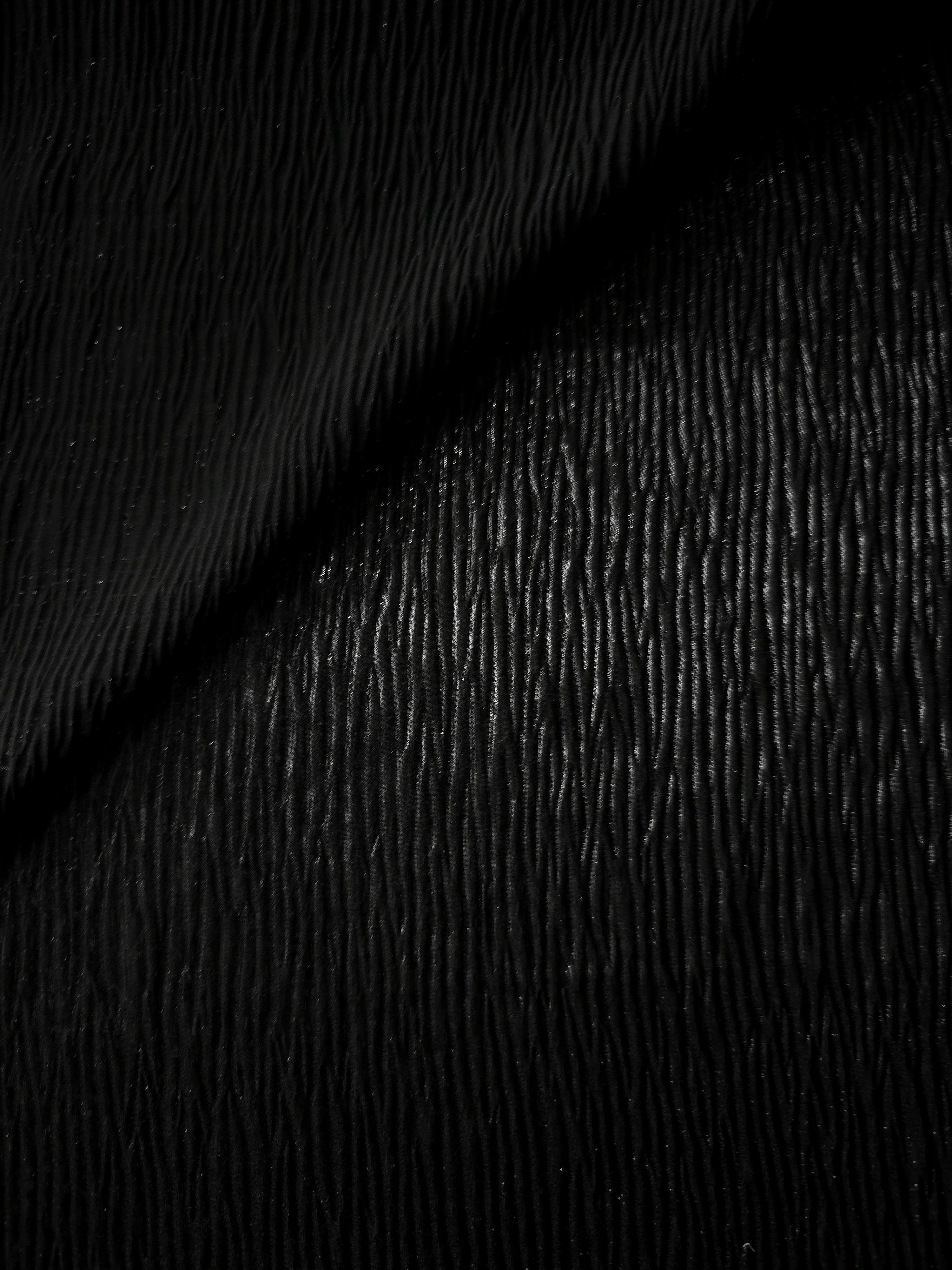 Fold detail of Jet Black fine mini-plissé fabric demonstrates how the textured surface builds depth for stagewear and layered fashion details.