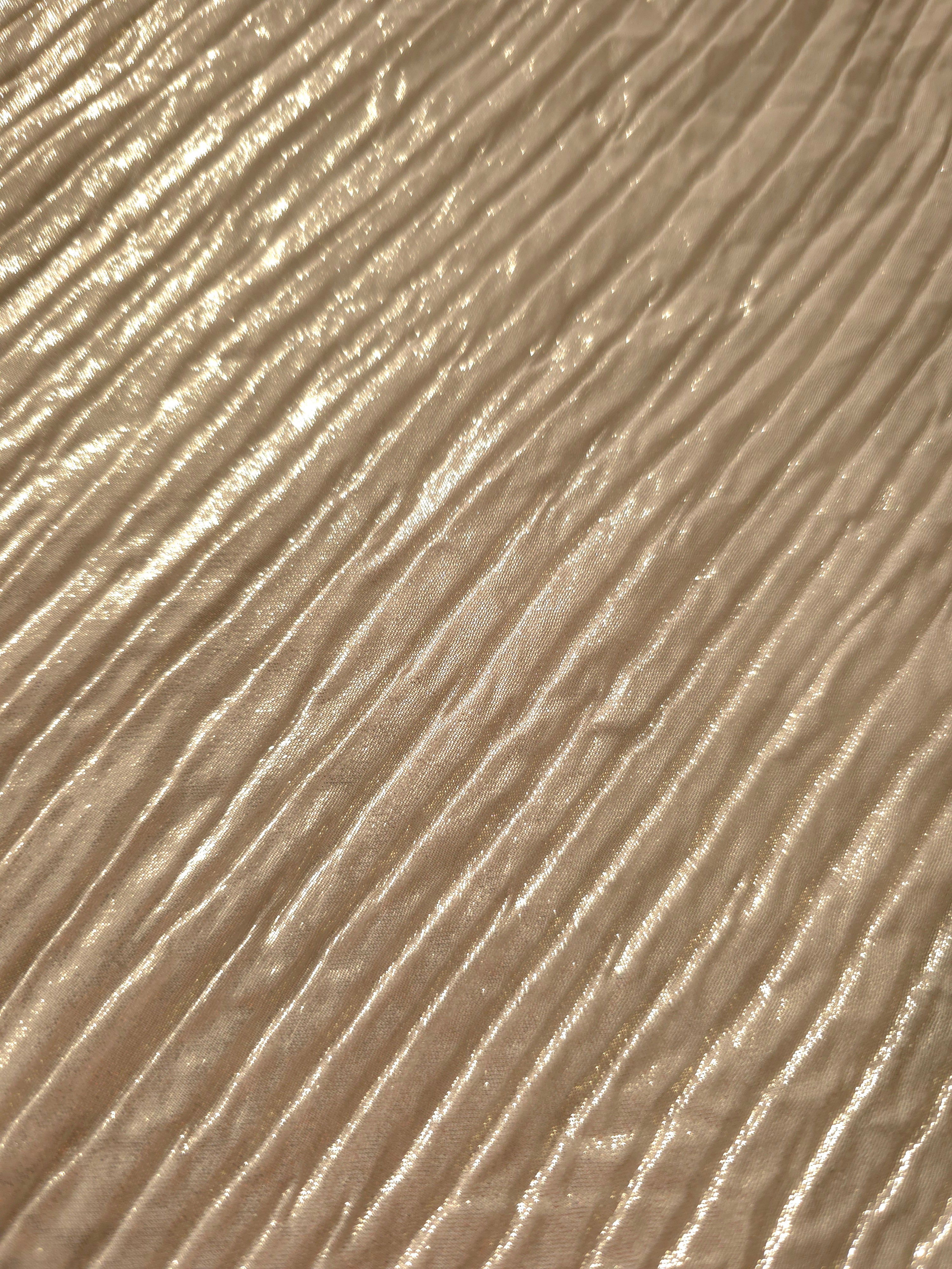 Soft drape of Champagne Beige textured shimmer plissé reveals dimensional folds and shifting reflection for jumpsuits and fluid occasionwear.