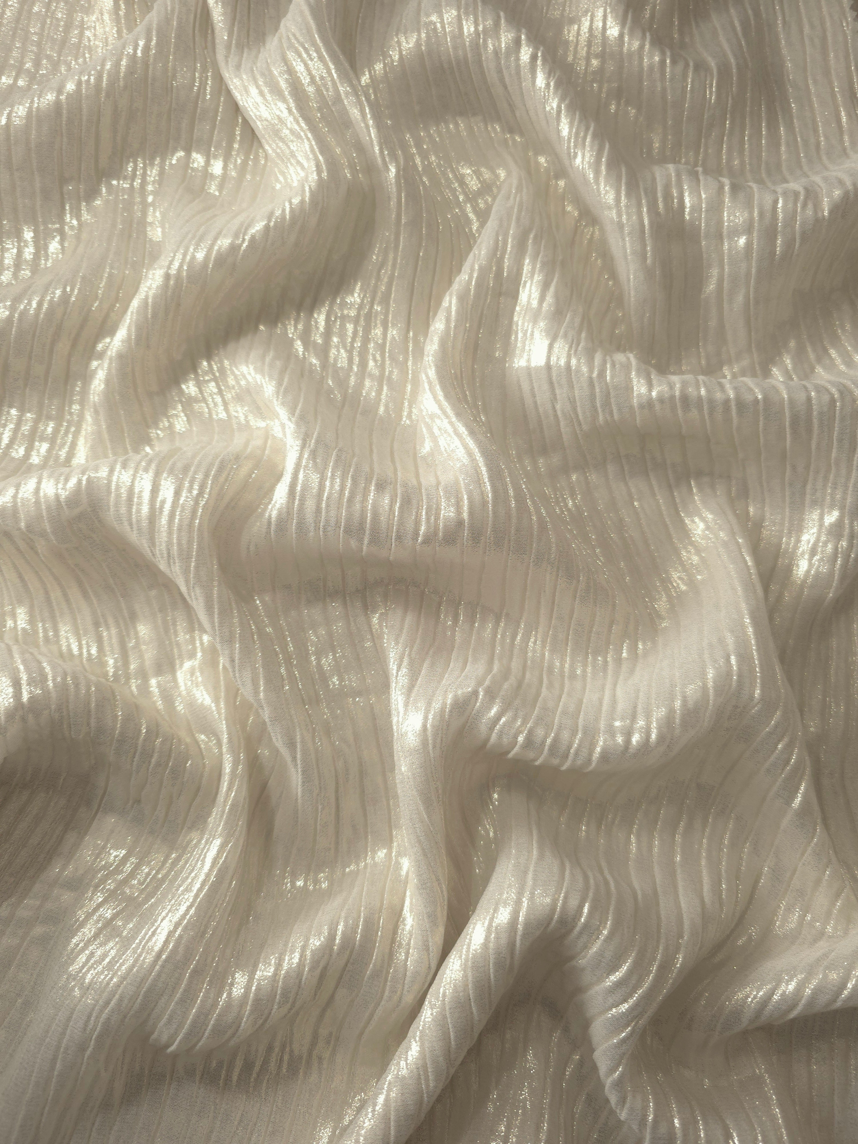 Flowing drape of Ivory Cream classic plissé shimmer fabric, showing regular pleated texture and light-catching movement for evening gowns and flowing maxi skirts.